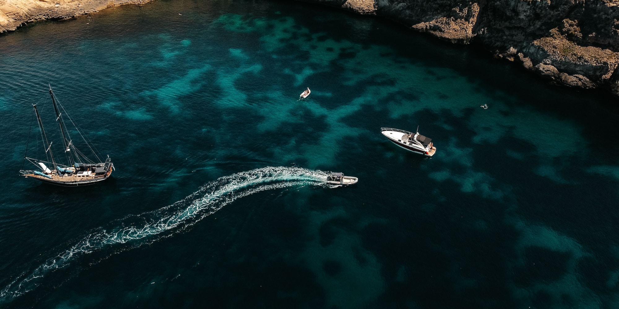 Aerial view of sailboat, yacht, speed boat in turquoise bay, rocky coast.