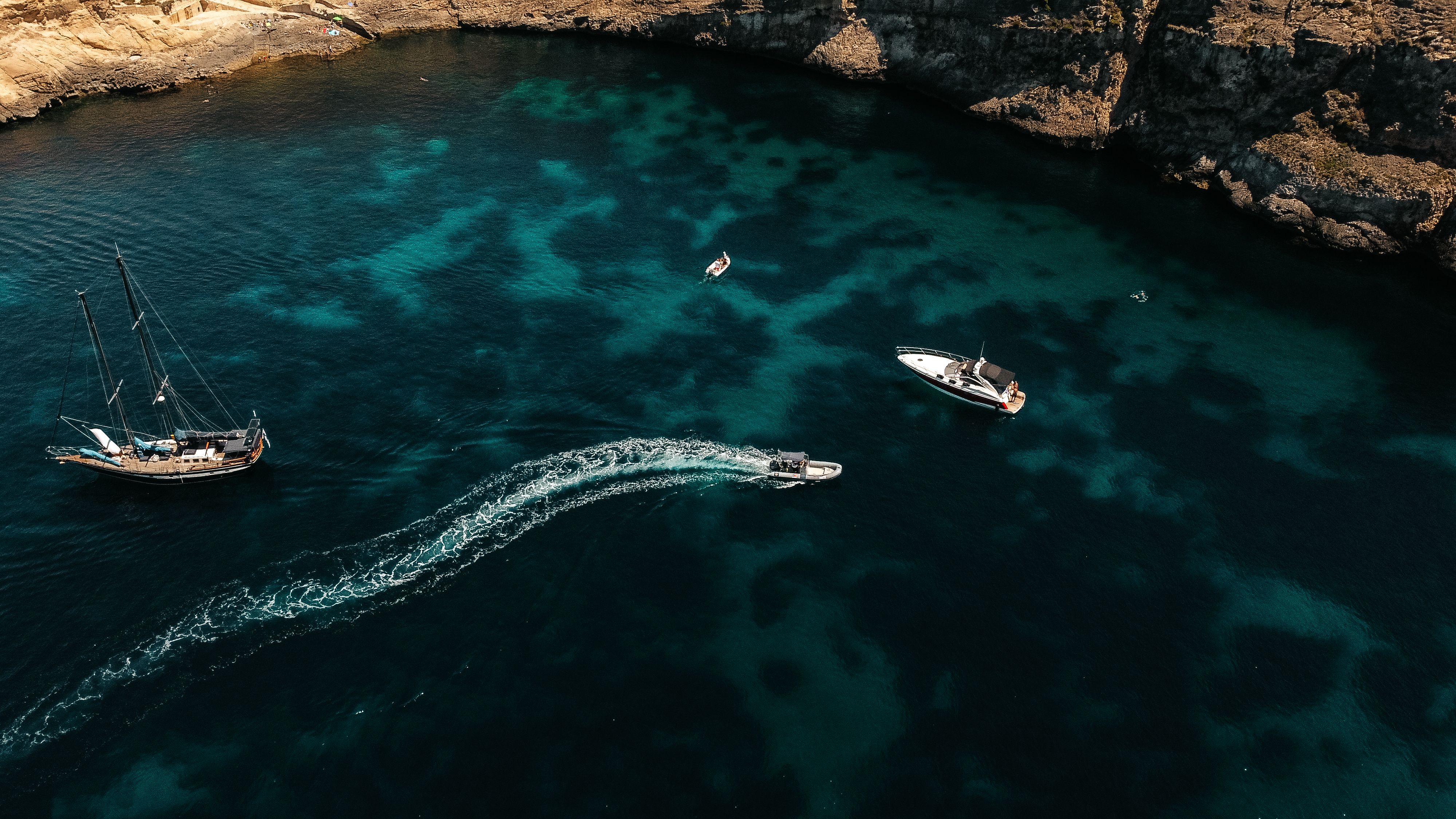 Aerial view of sailboat, yacht, speed boat in turquoise bay, rocky coast.