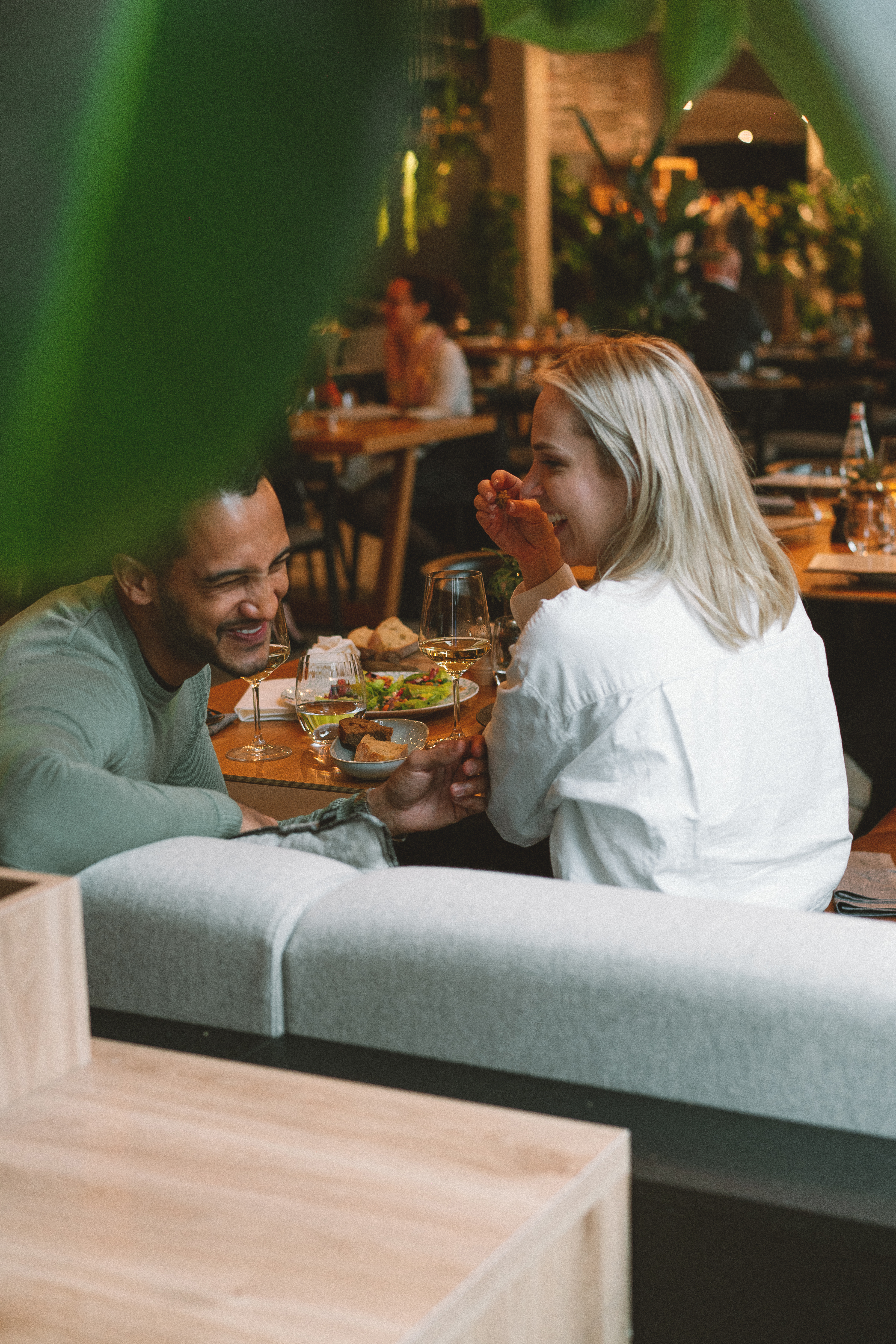 Couple laughing and holding hands at a restaurant table with wine and food.