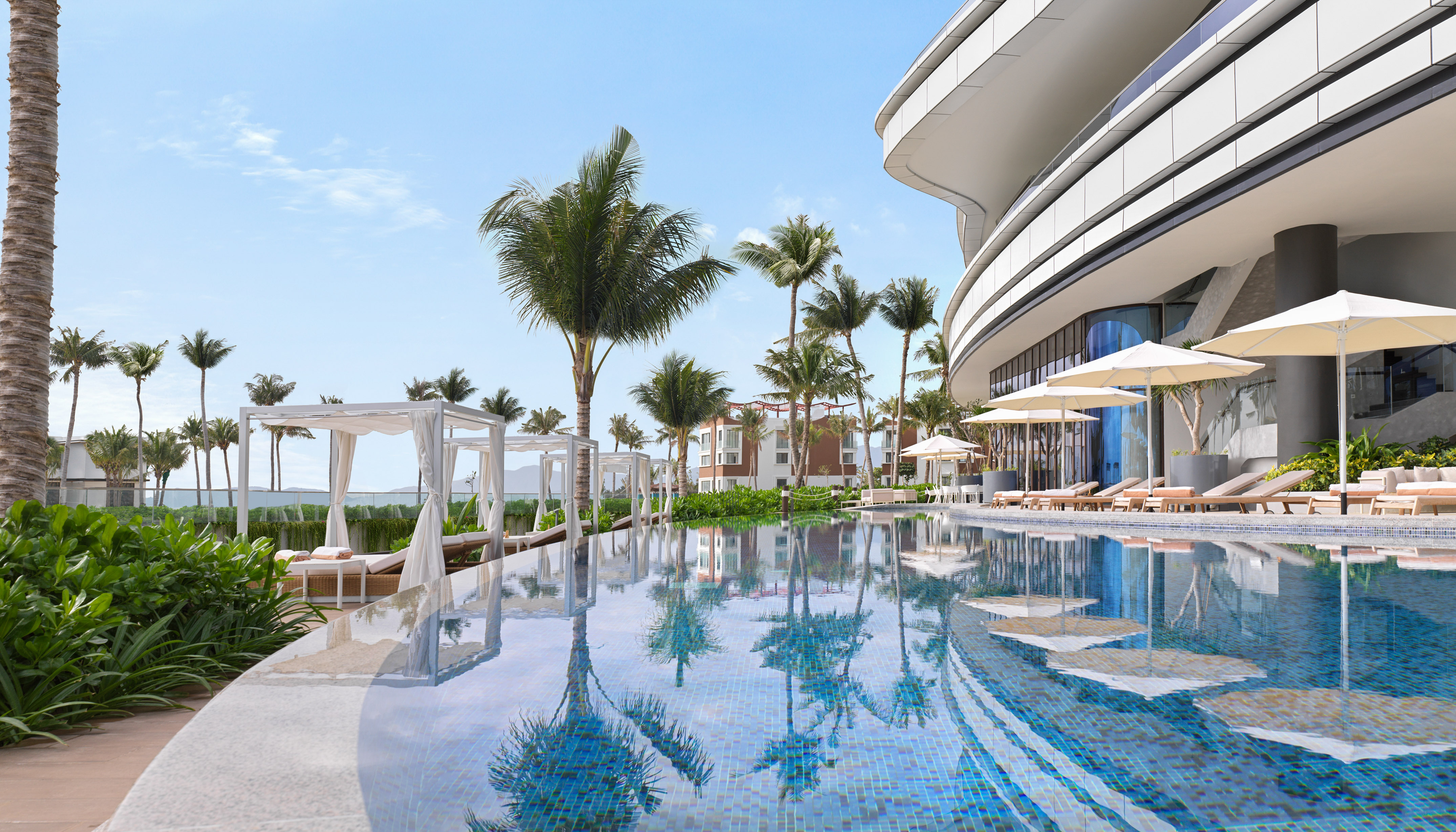 Tropical resort pool with palm trees, white cabanas, and curved modern hotel.