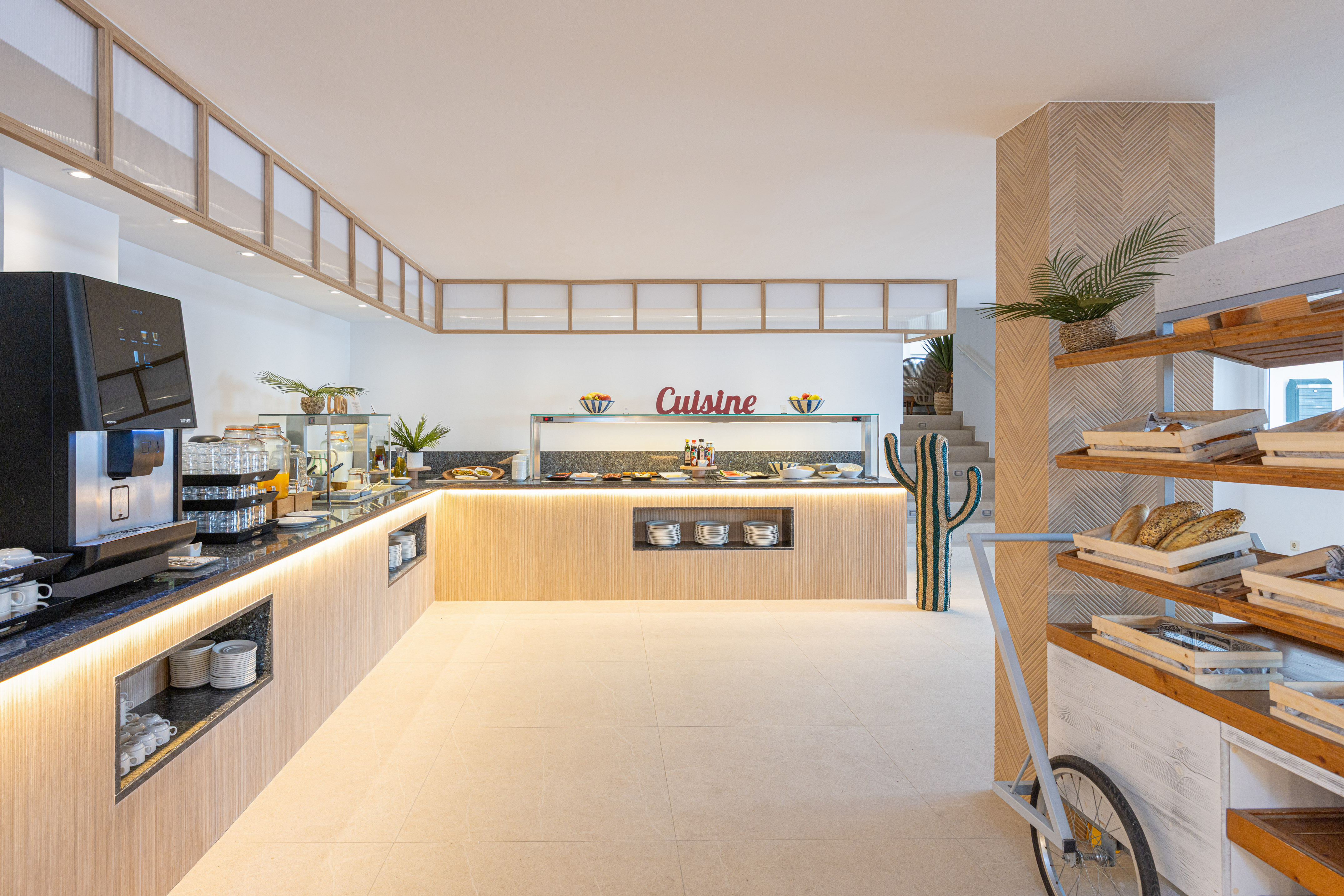 Modern hotel breakfast buffet with food display, coffee machine, and bread cart.