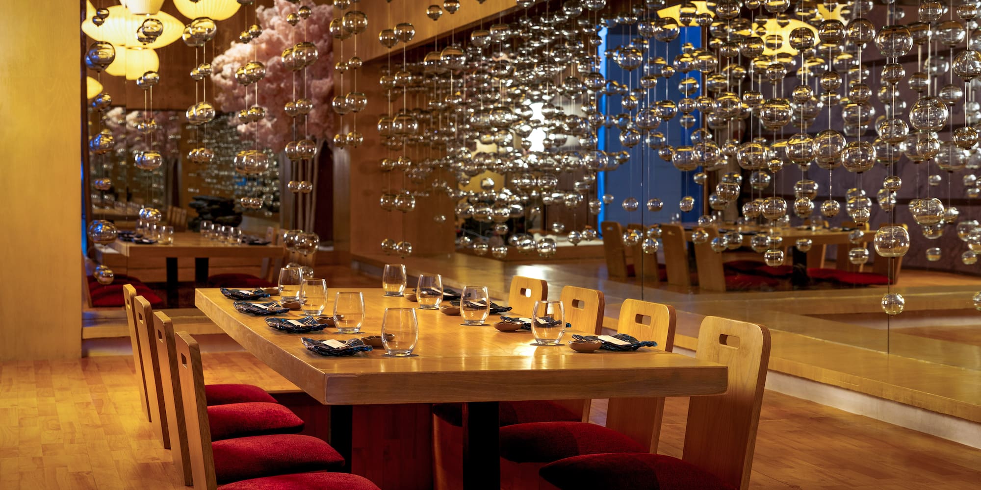 Japanese dining room with wooden table, red cushions, and hanging glass decor.