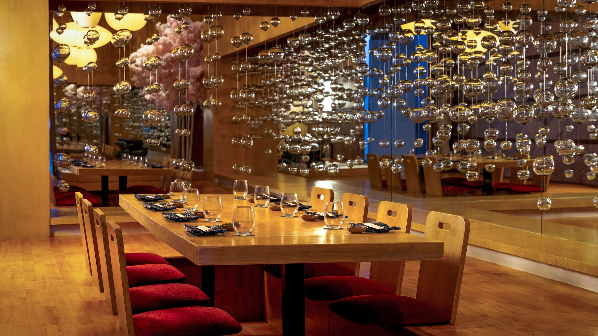 Japanese dining room with wooden table, red cushions, and hanging glass decor.