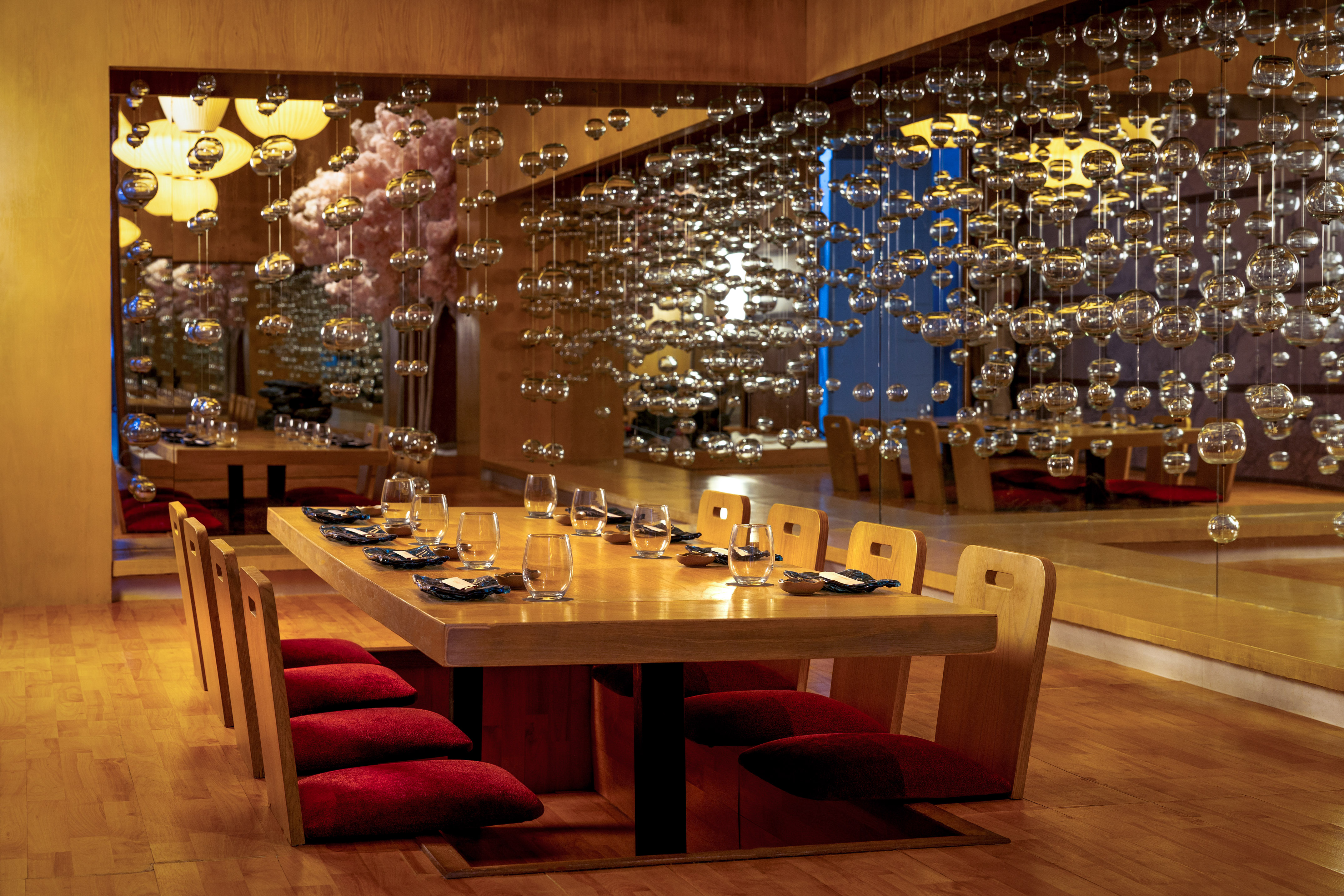 Japanese dining room with wooden table, red cushions, and hanging glass decor.