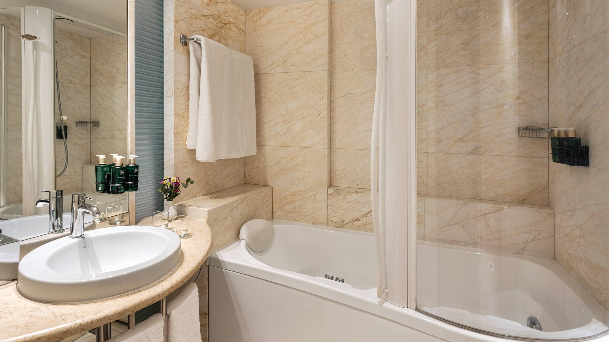 Elegant marble bathroom with white sink, bathtub, and shower.