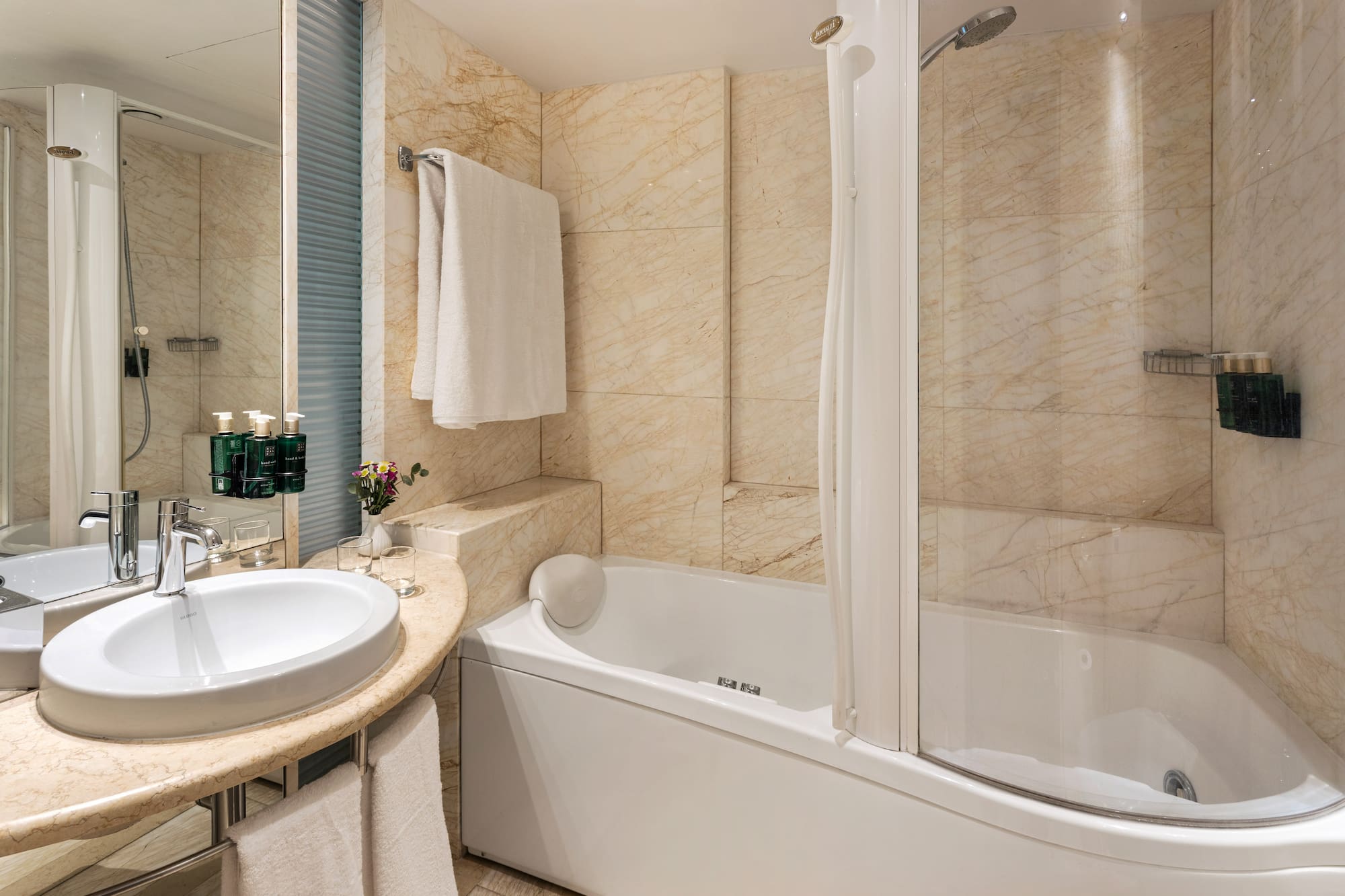 Elegant marble bathroom with white sink, bathtub, and shower.