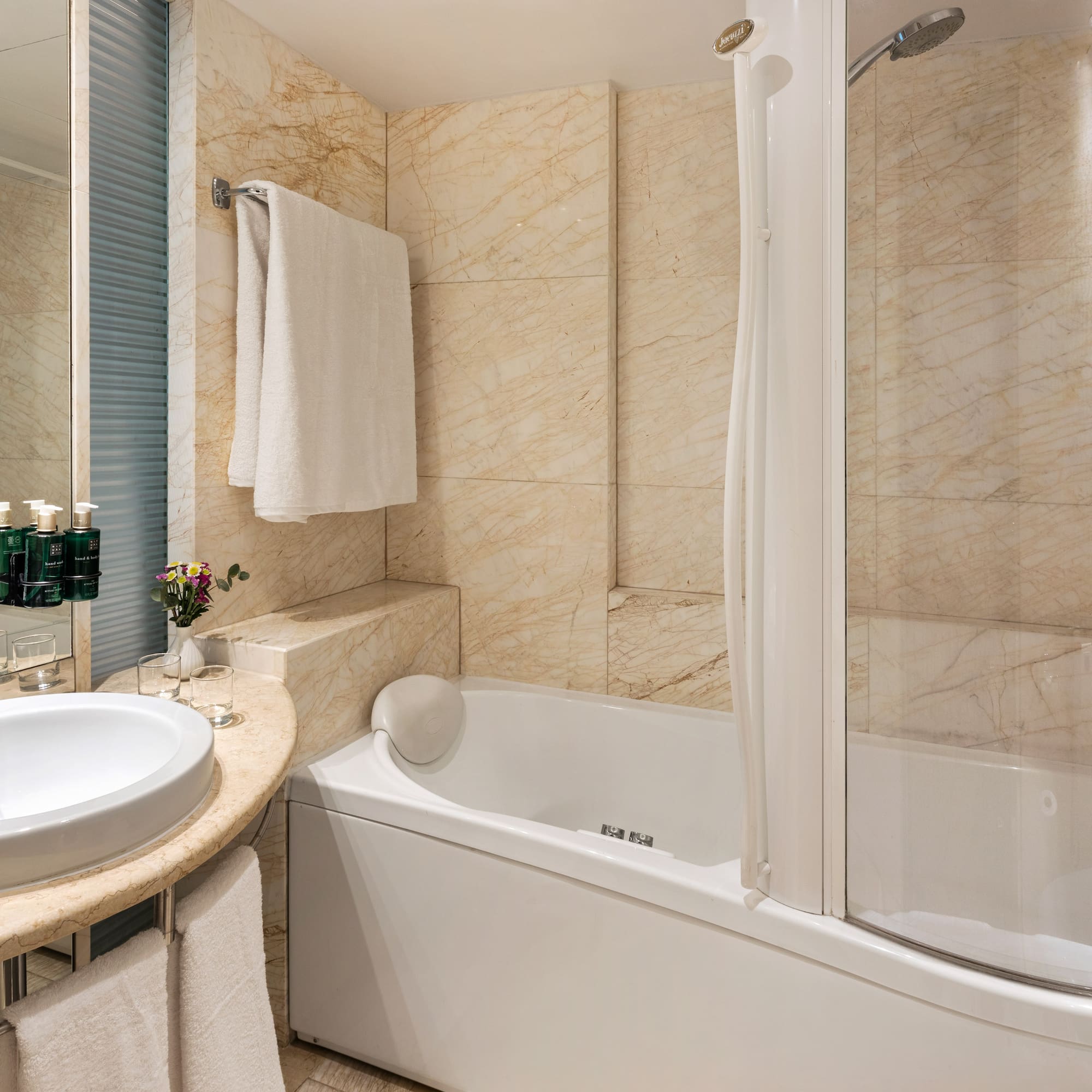 Elegant marble bathroom with white sink, bathtub, and shower.