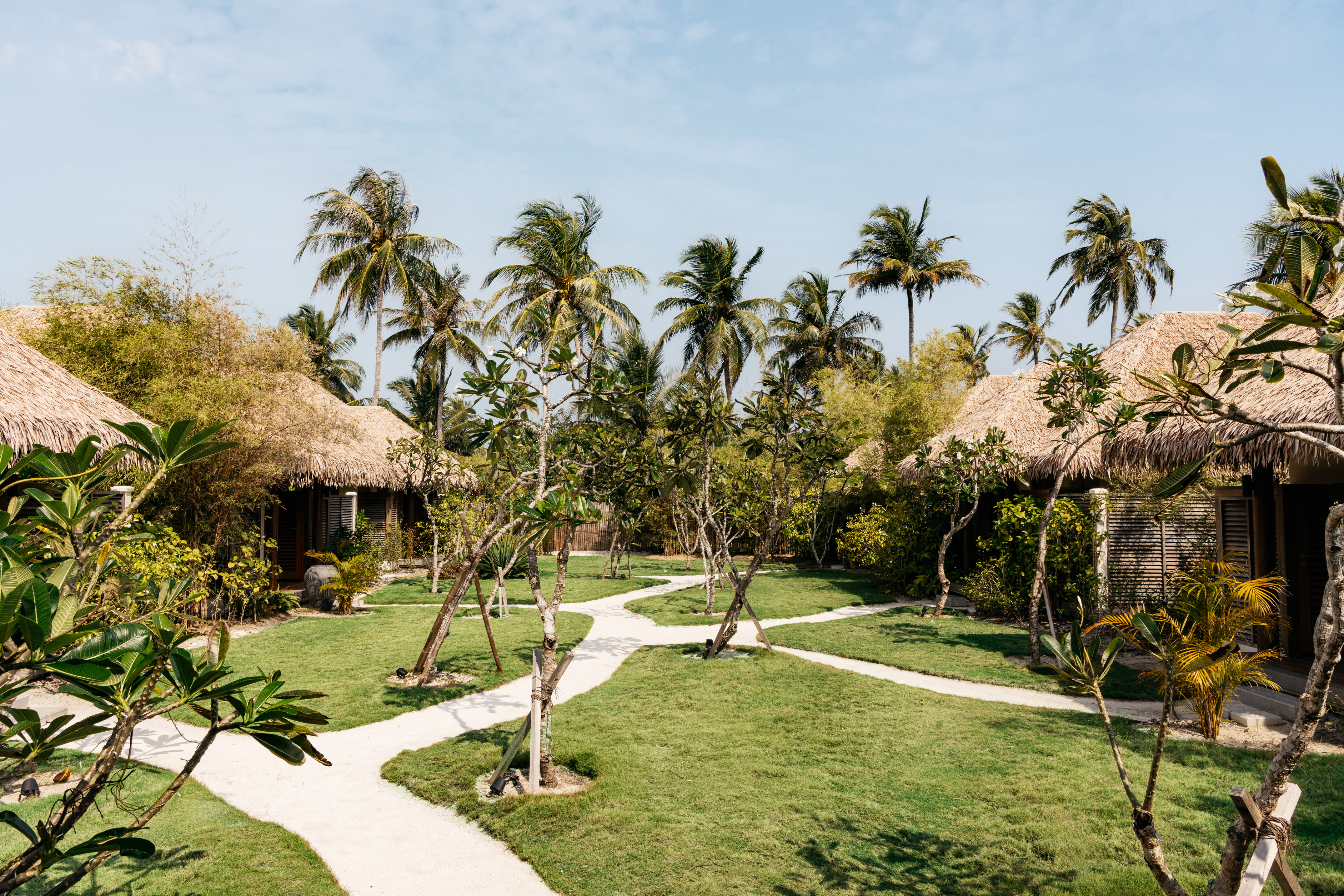 Tropical resort villas with thatched roofs, palm trees, and winding paths.