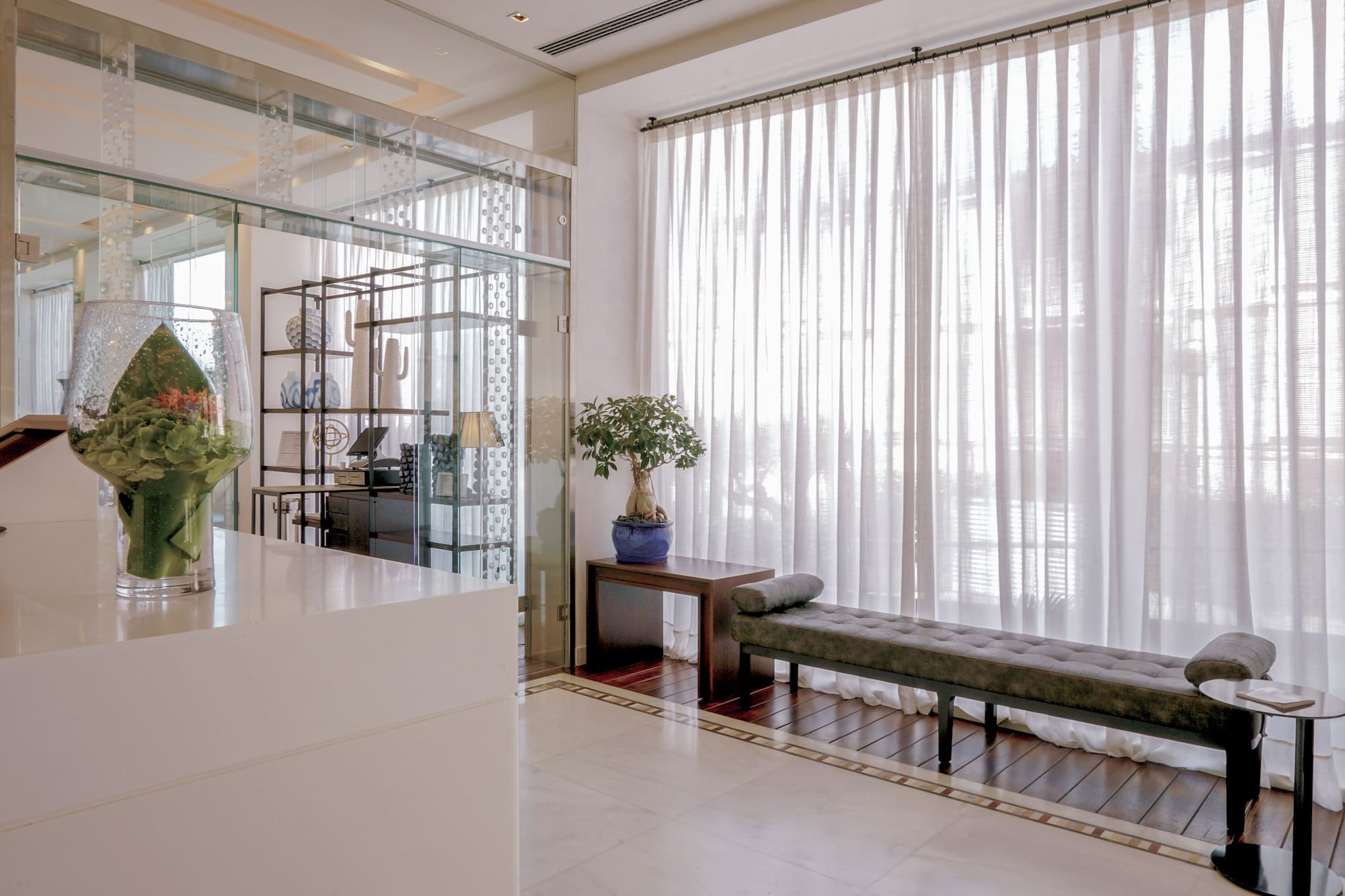 Modern reception lobby with glass partition, sheer curtains, and a waiting bench.