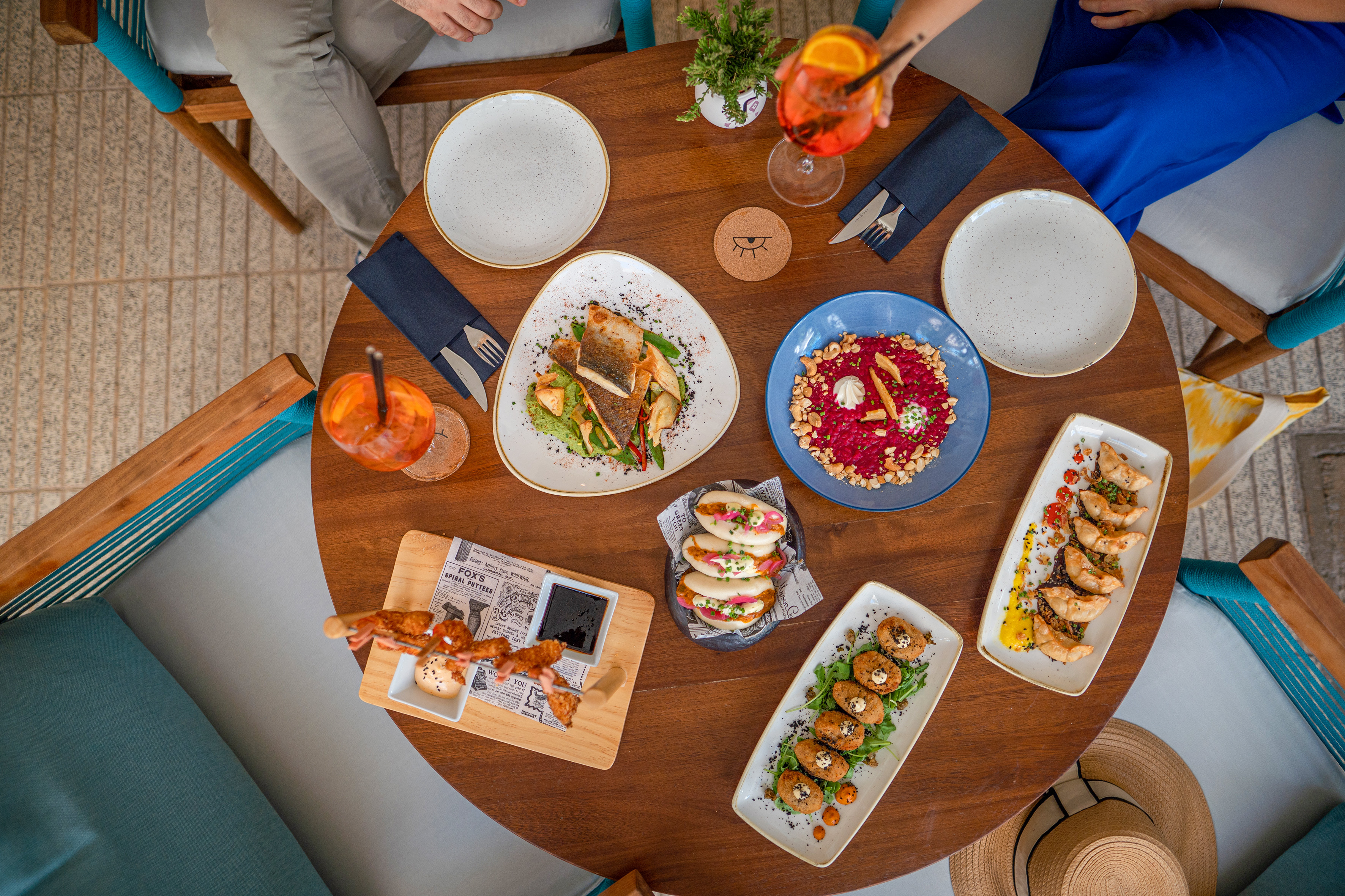 Restaurant table with diverse dishes: fish, bao buns, dumplings, and cocktails.