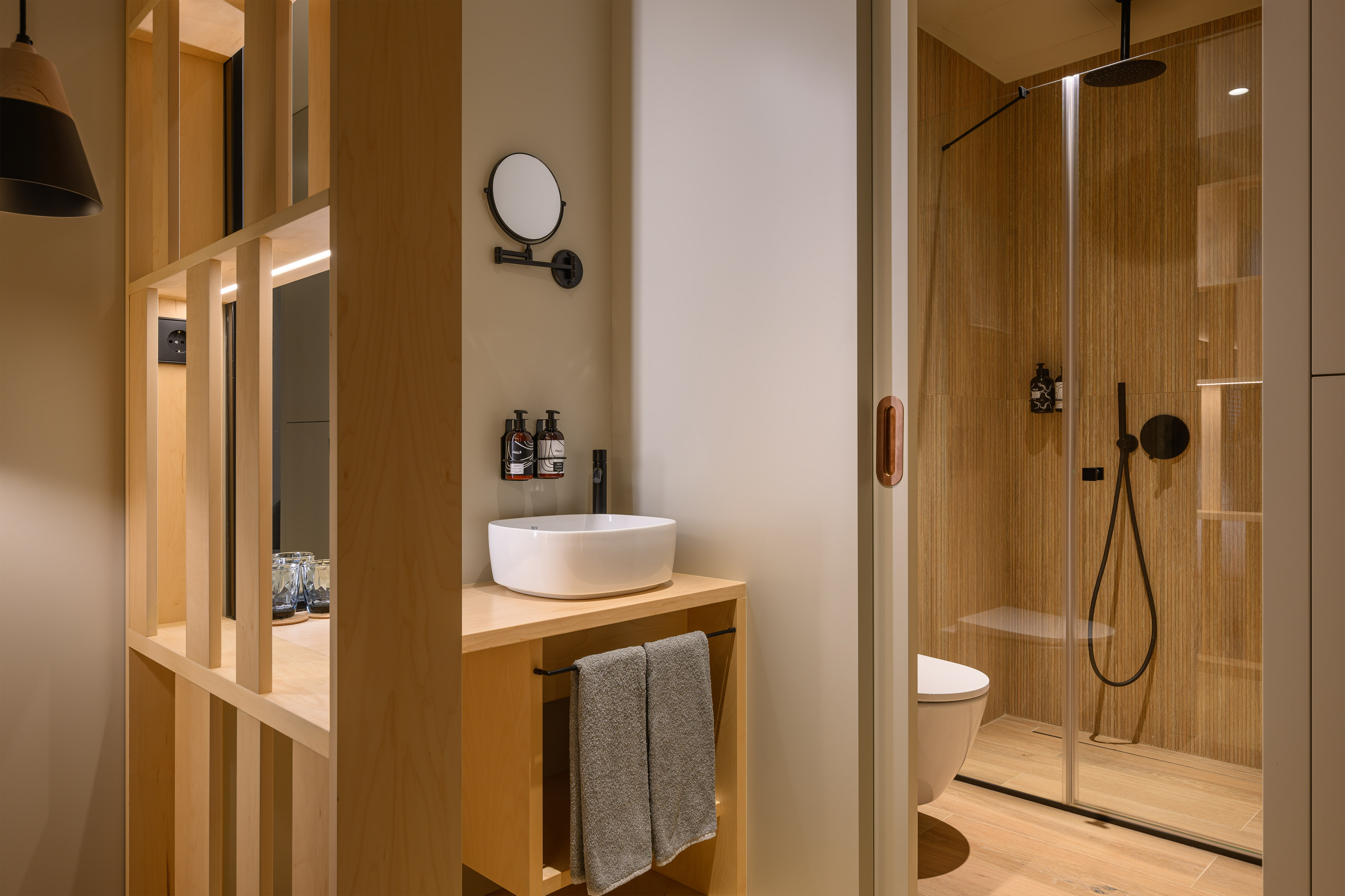 Modern wooden bathroom with vessel sink, black fixtures, and glass shower.