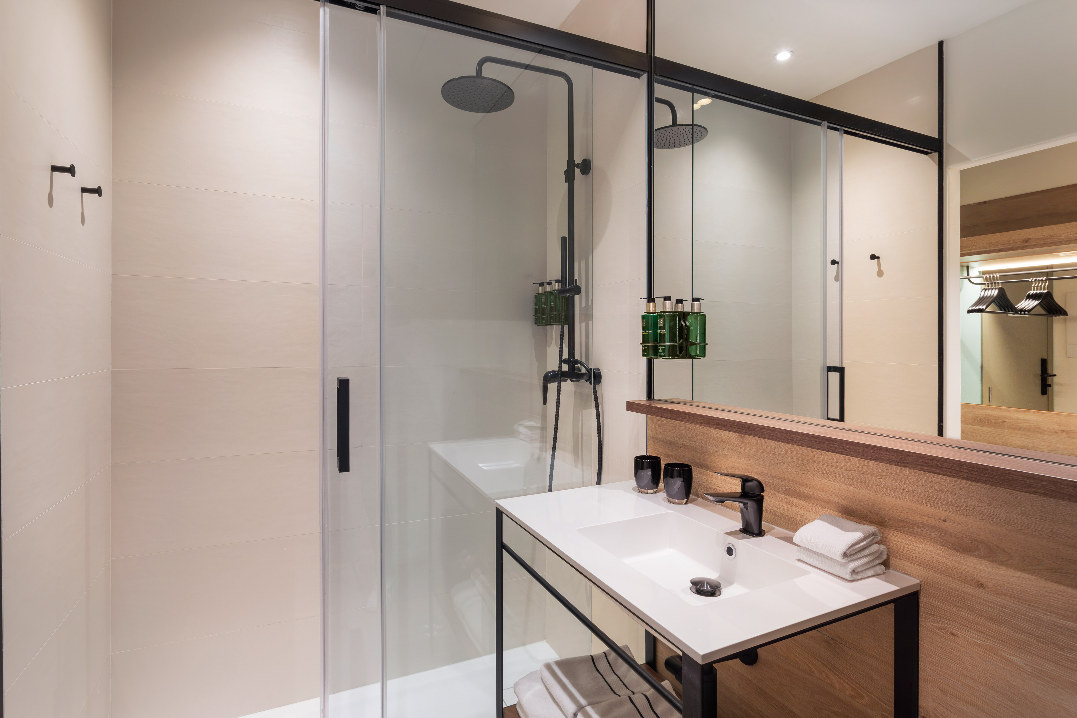 Modern hotel bathroom: glass shower, black rain shower, white sink, wood vanity.