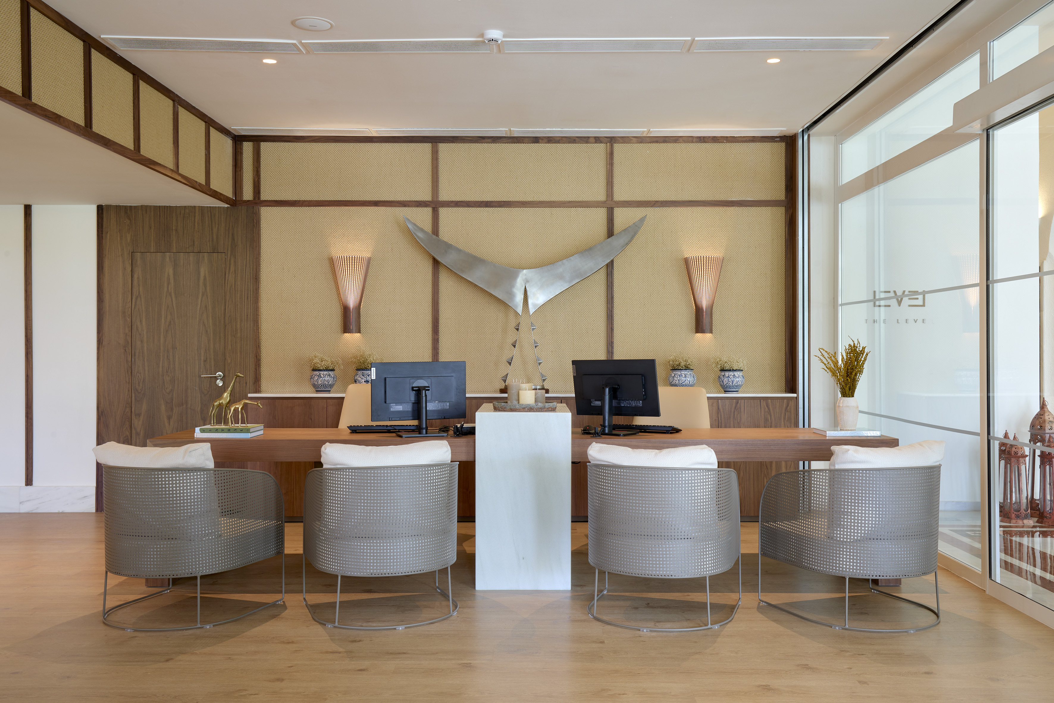 Modern luxury reception desk with monitors, stylish chairs, and textured wall art.