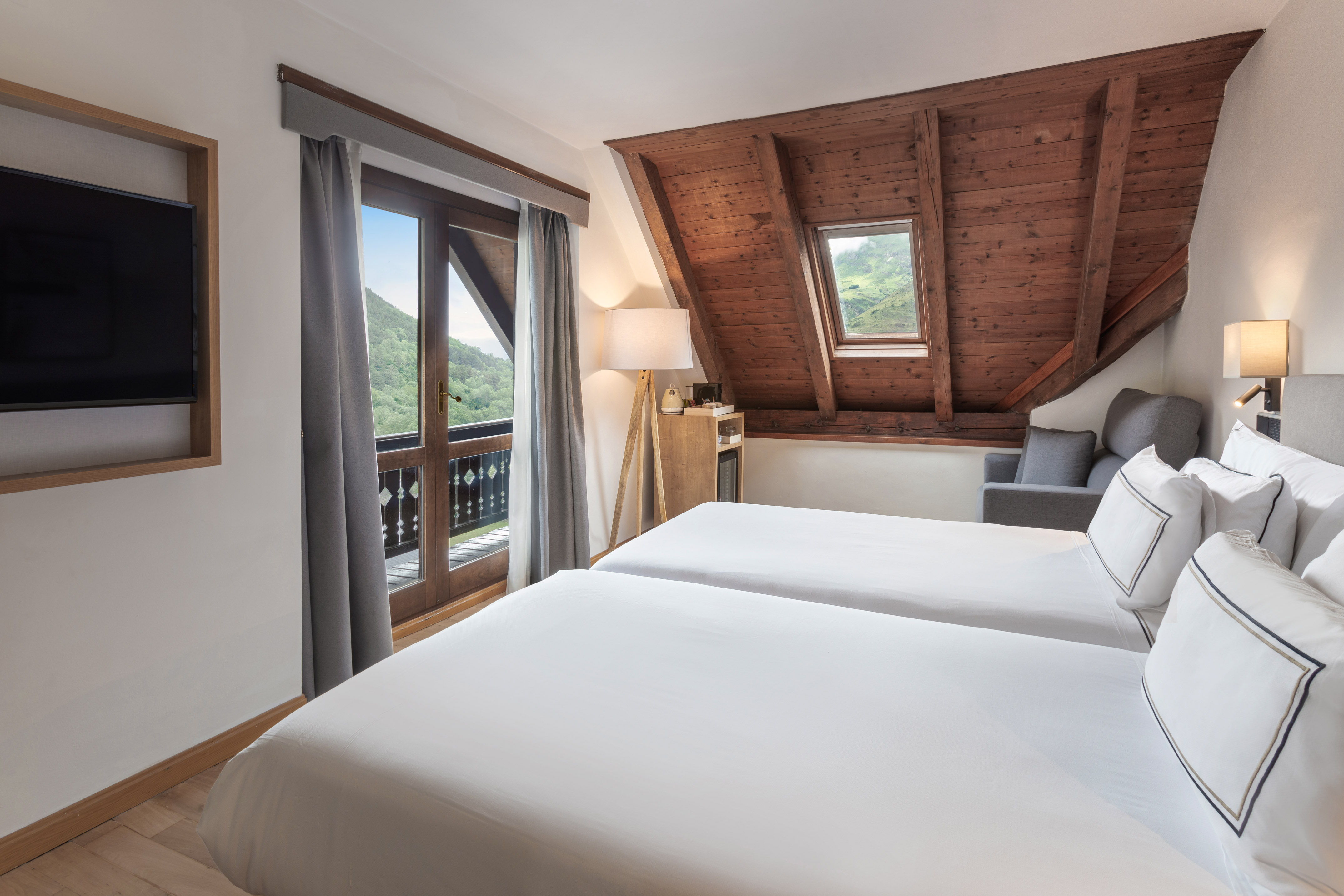 Hotel room with twin beds, mountain view balcony, and wooden ceiling.