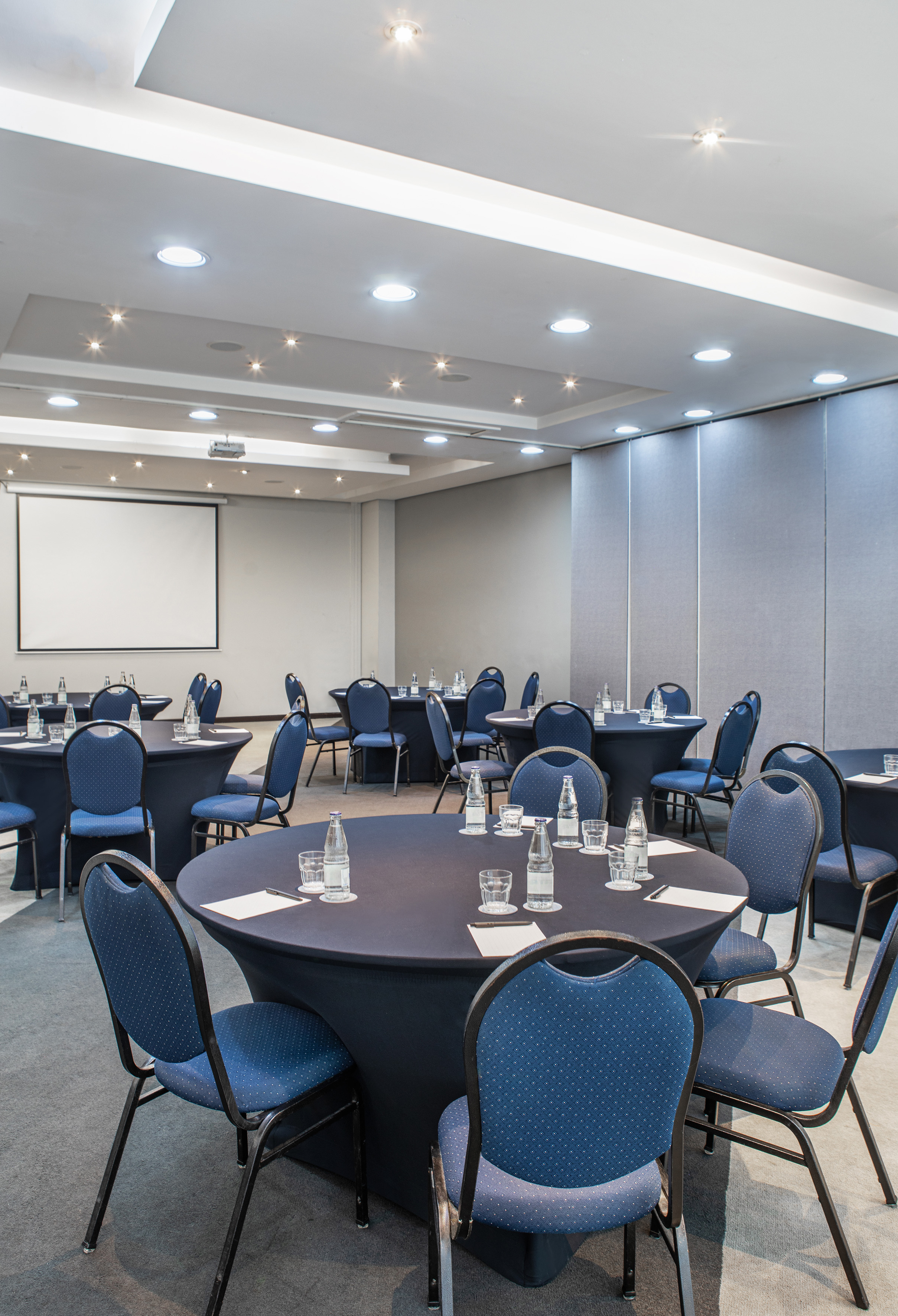 Business meeting room with round tables, blue chairs, projector screen.