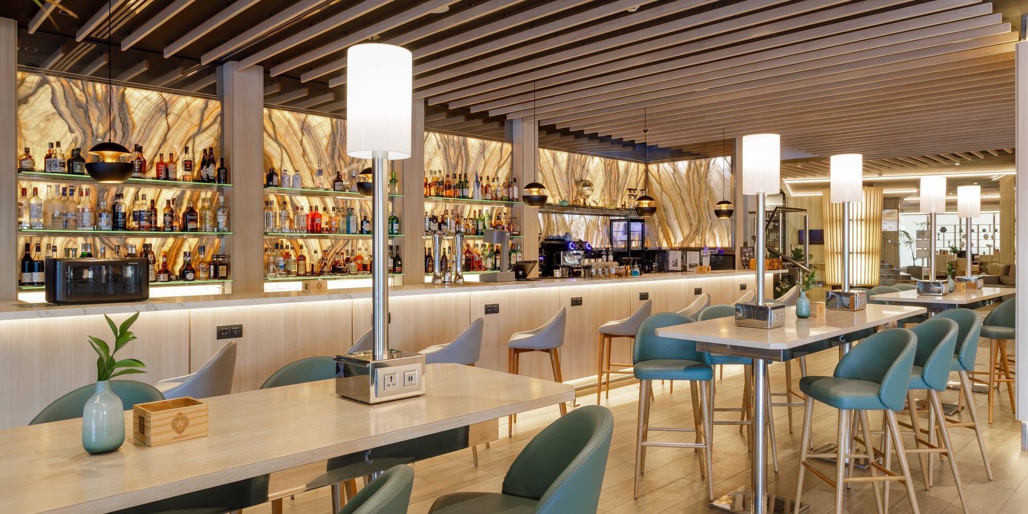 Elegante bar moderno con barra de licores, mesas altas y sillas verdes.