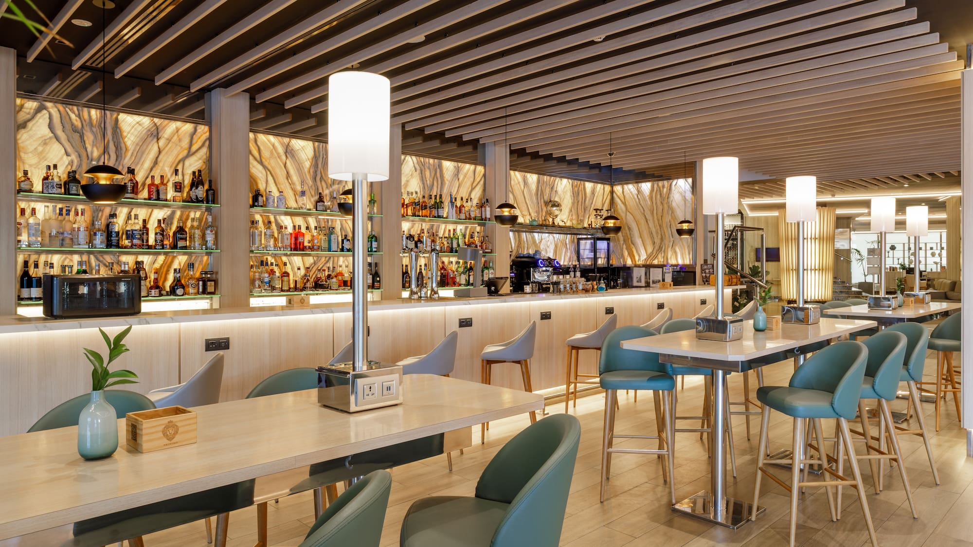 Elegante bar moderno con barra de licores, mesas altas y sillas verdes.