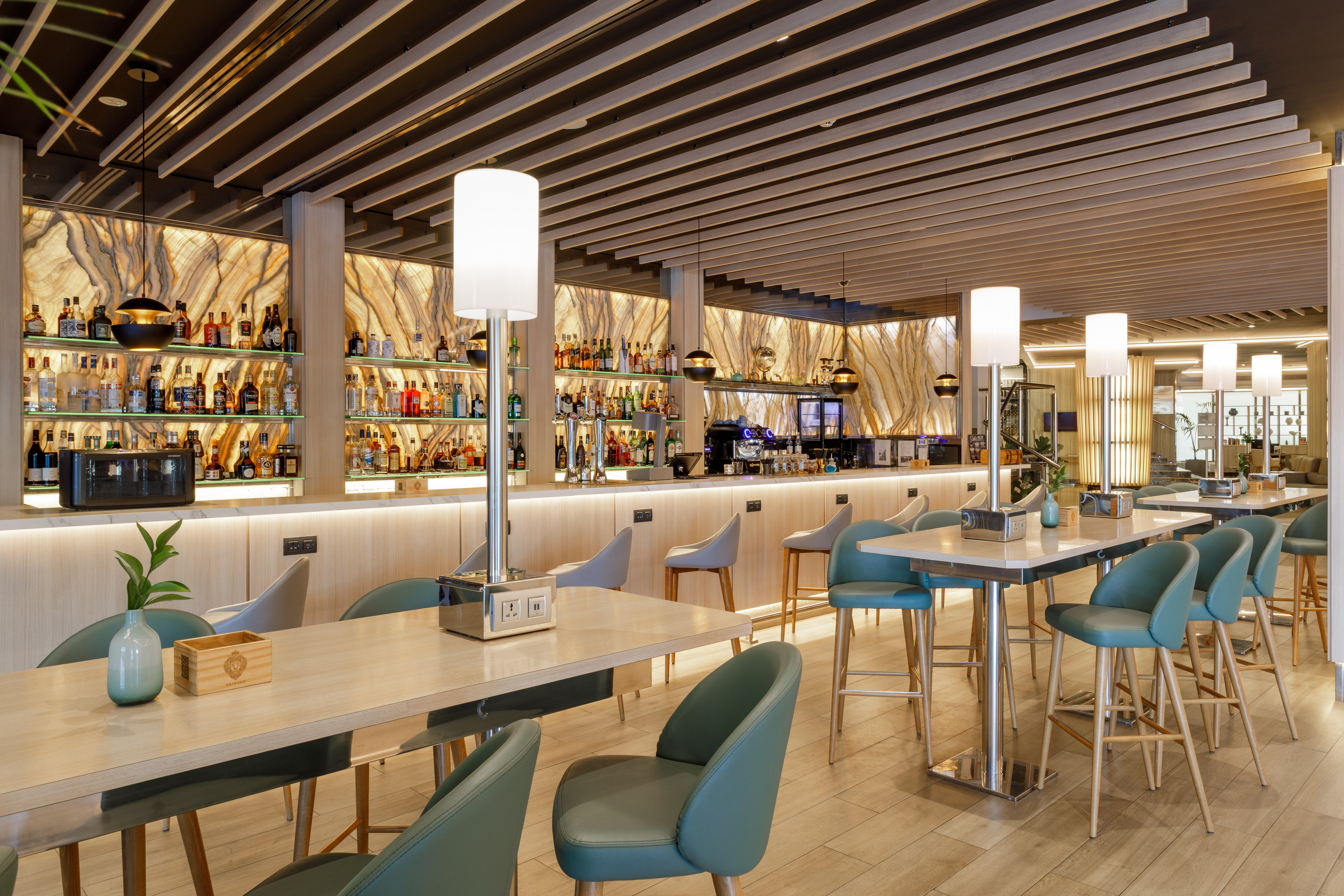 Elegante bar moderno con barra de licores, mesas altas y sillas verdes.