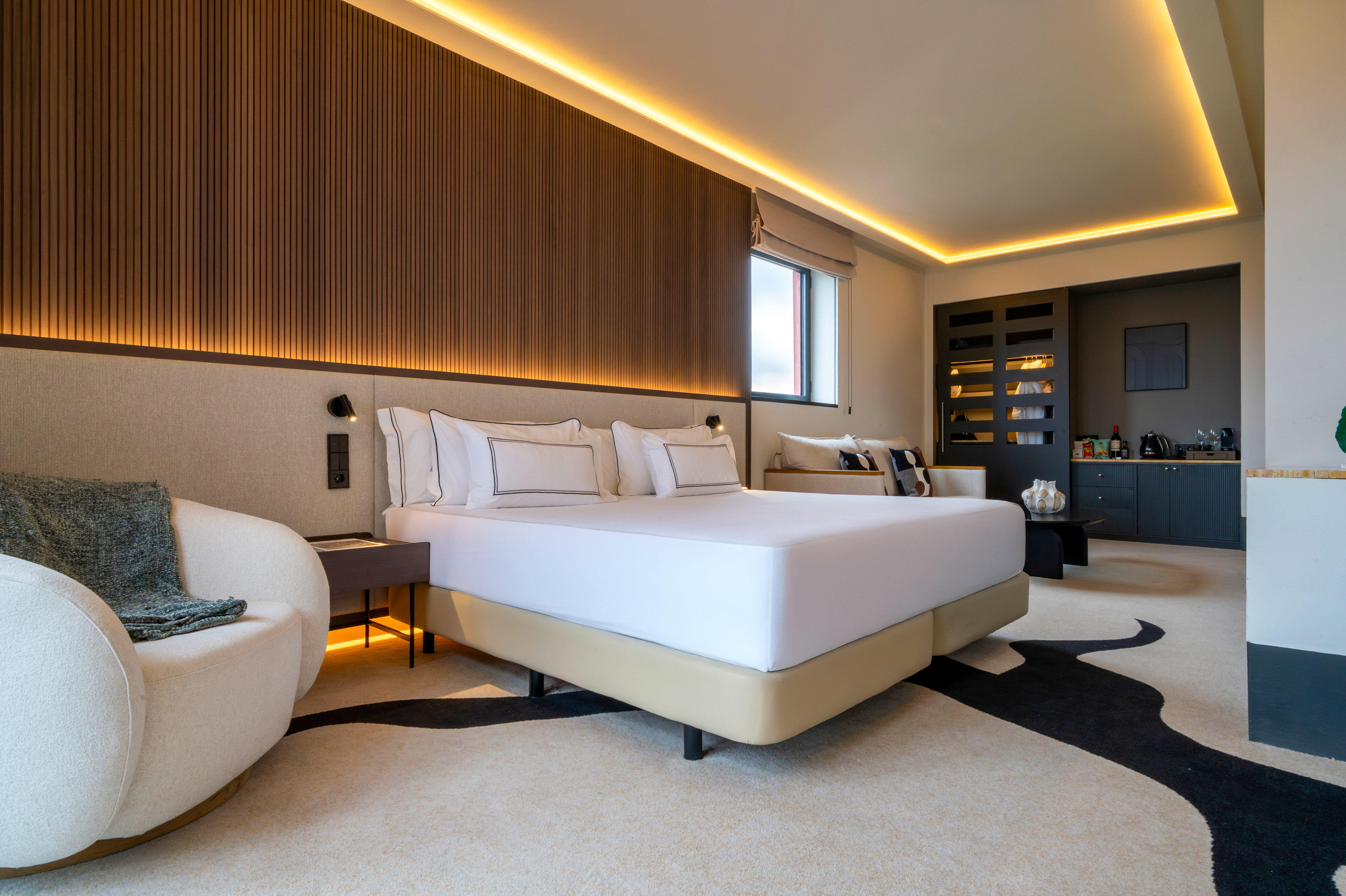 Modern hotel room with white bed, wooden accent wall, ambient lighting, and modern decor.