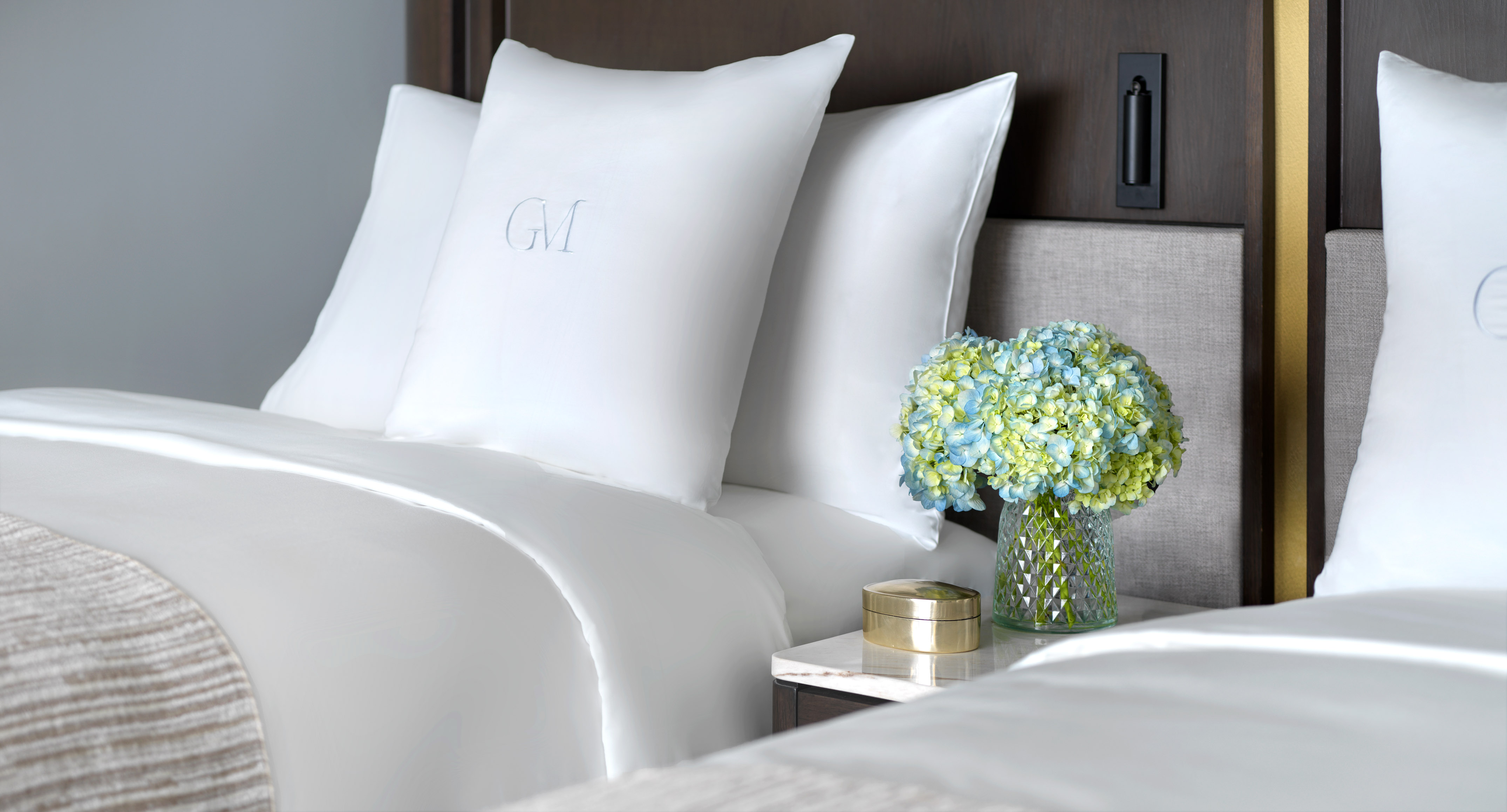 Hotel room with white monogrammed bedding, blue hydrangeas on nightstand.