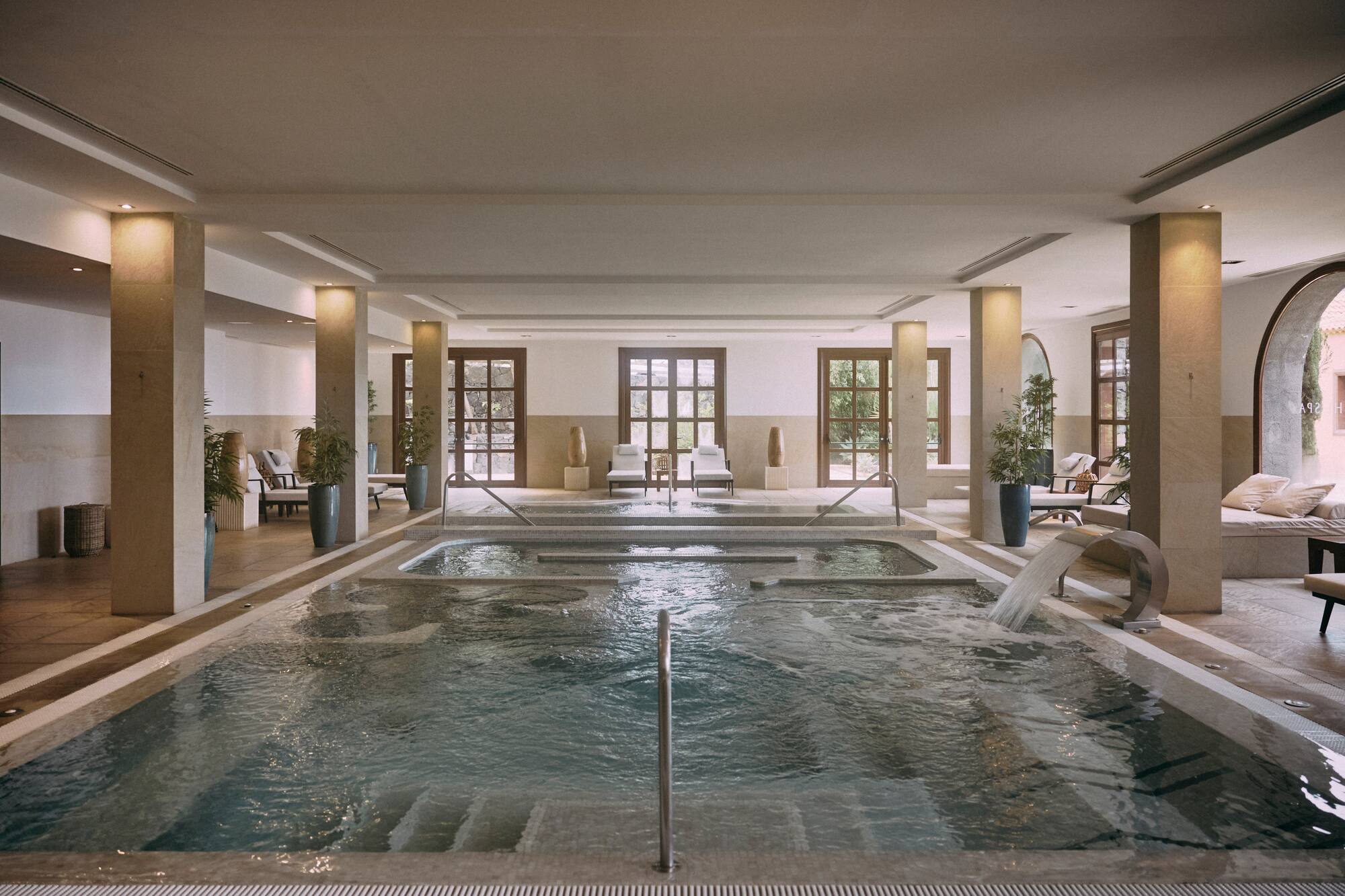Indoor luxury spa pool with hydrotherapy features and lounge chairs.