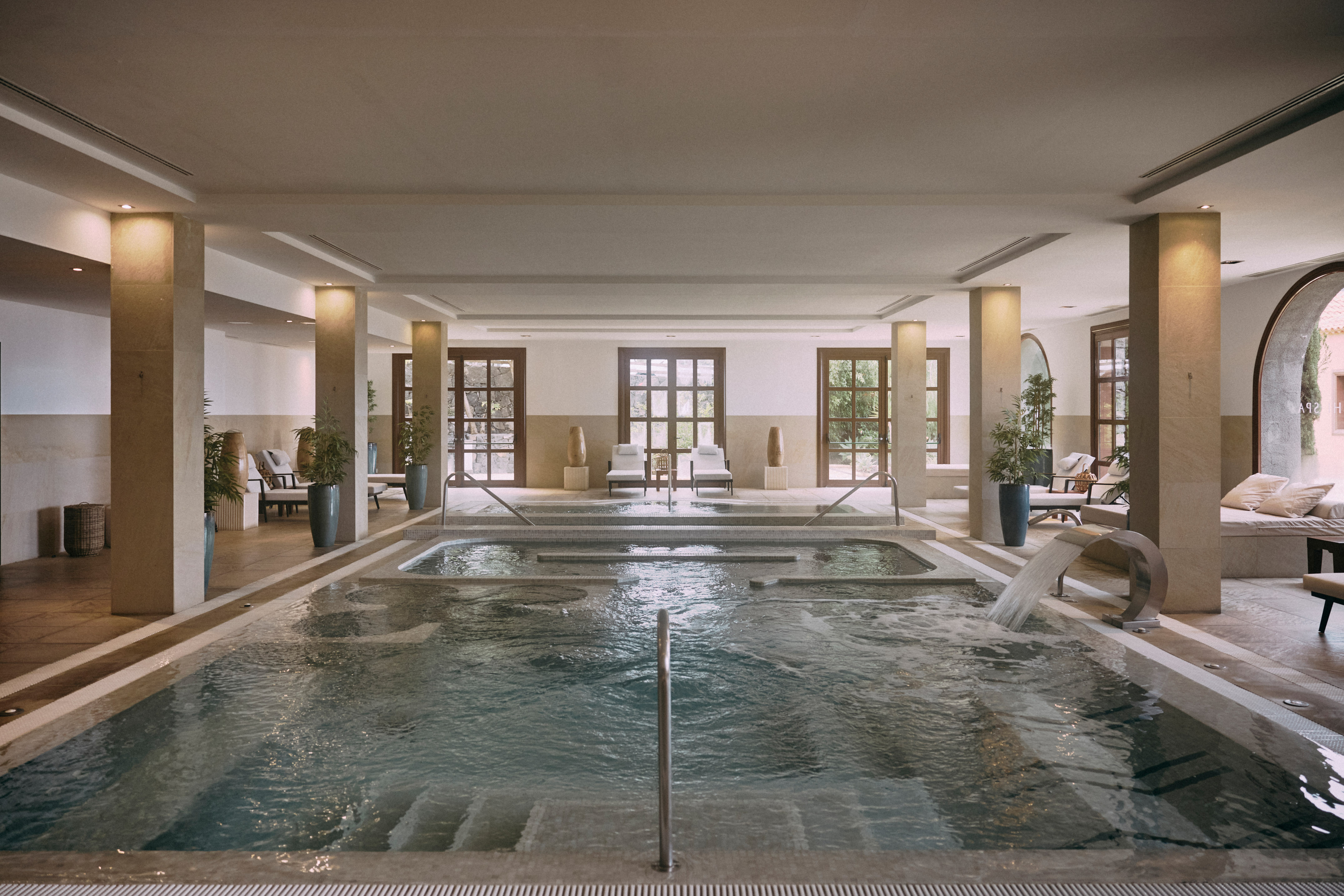 Indoor luxury spa pool with hydrotherapy features and lounge chairs.