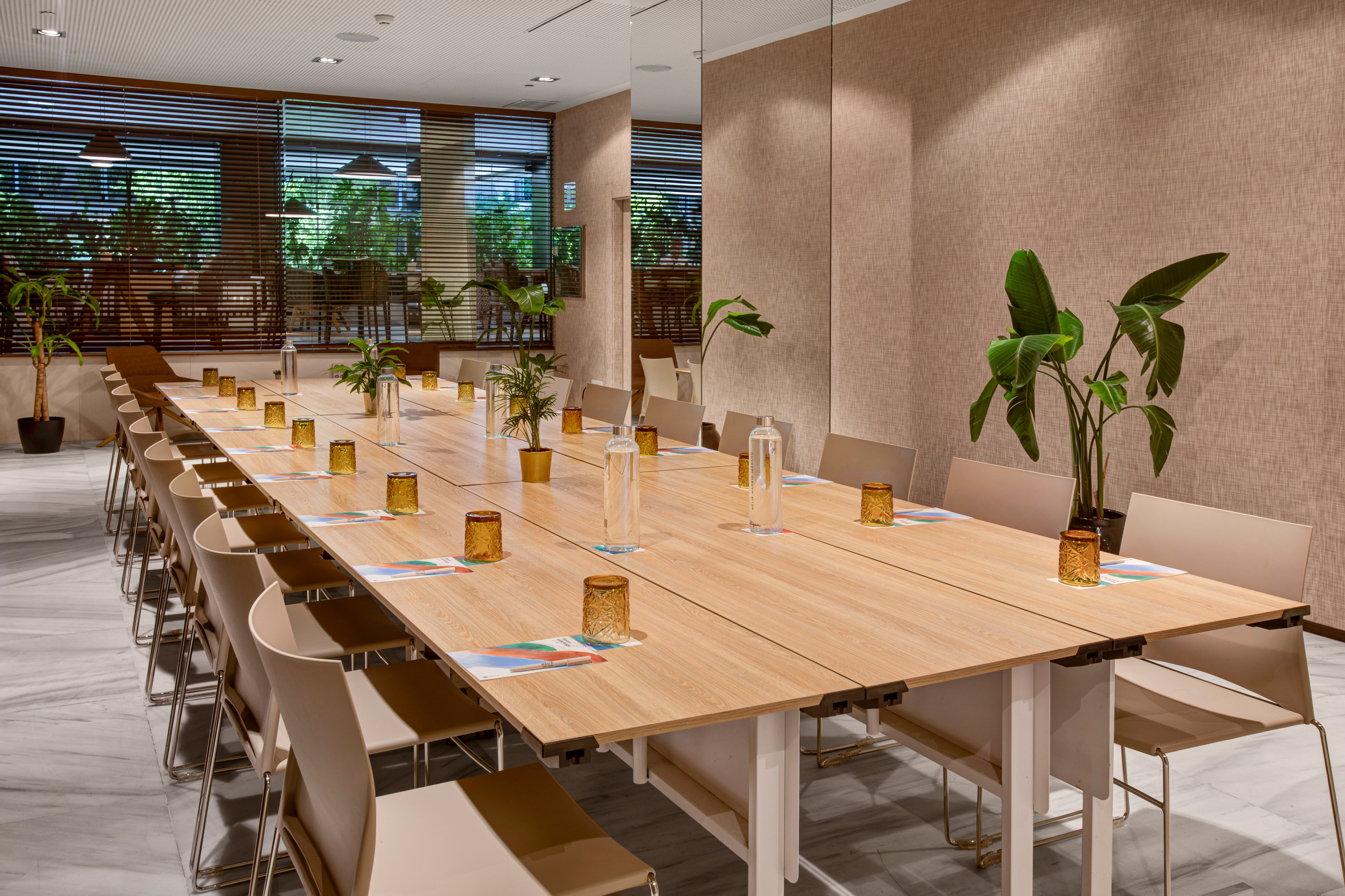 Elegant meeting room with long wooden table, chairs, and potted greenery.