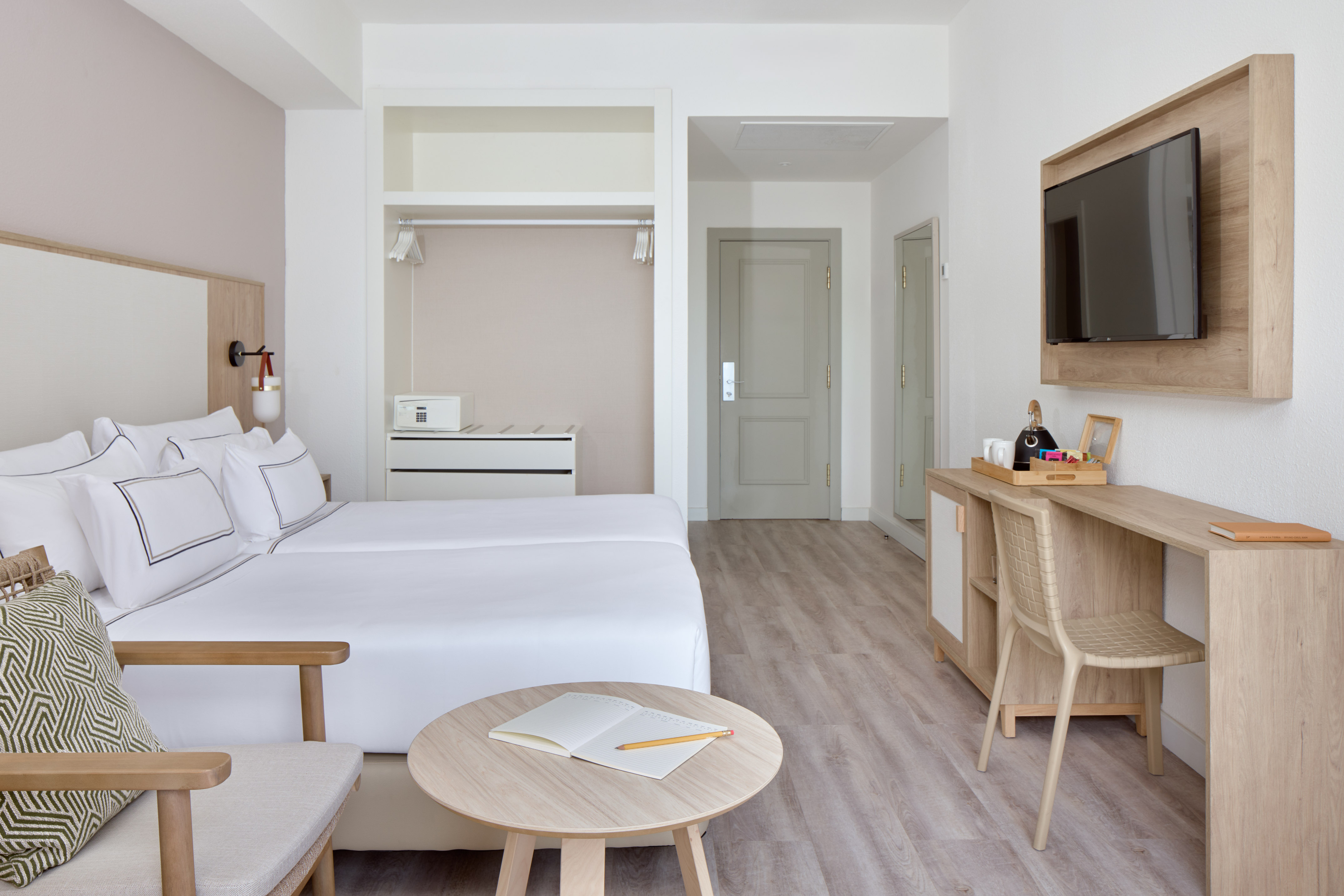 Modern hotel room with twin beds, desk, TV, and minimalist wood furniture.