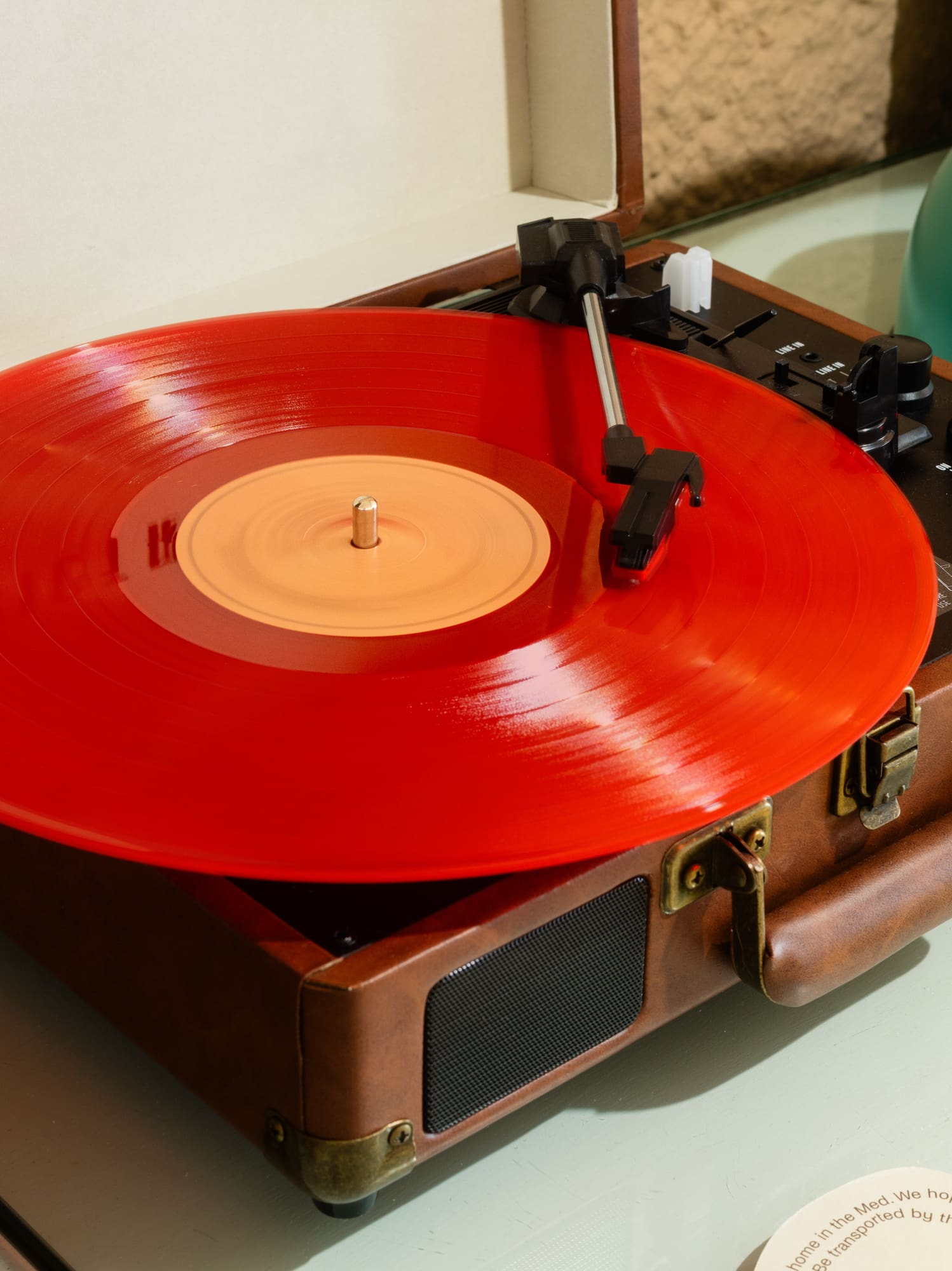 Tocadiscos de maleta con vinilo rojo. Detrás, tetera turquesa.