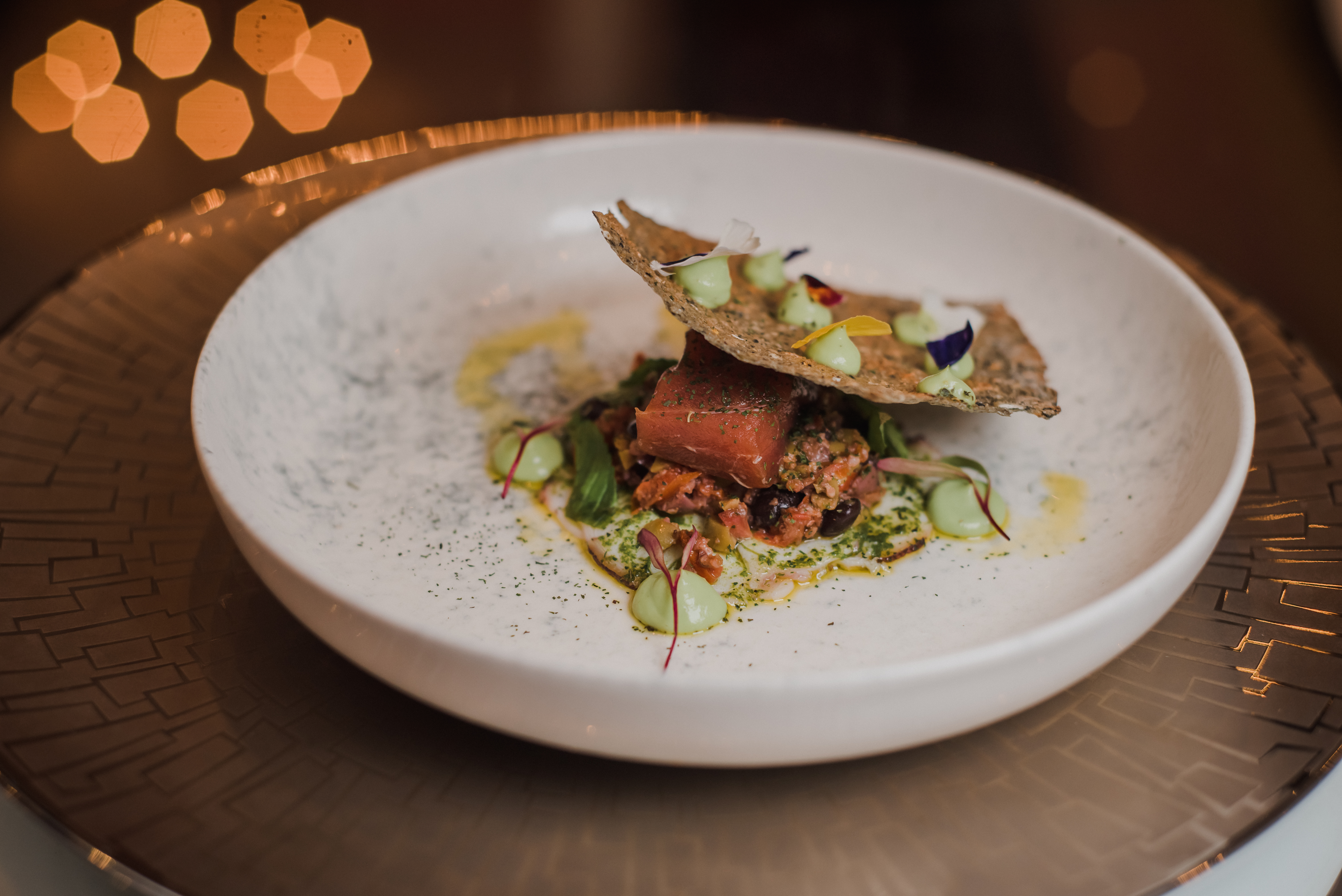 Fine dining fish dish with cracker, green sauce, and floral garnish.