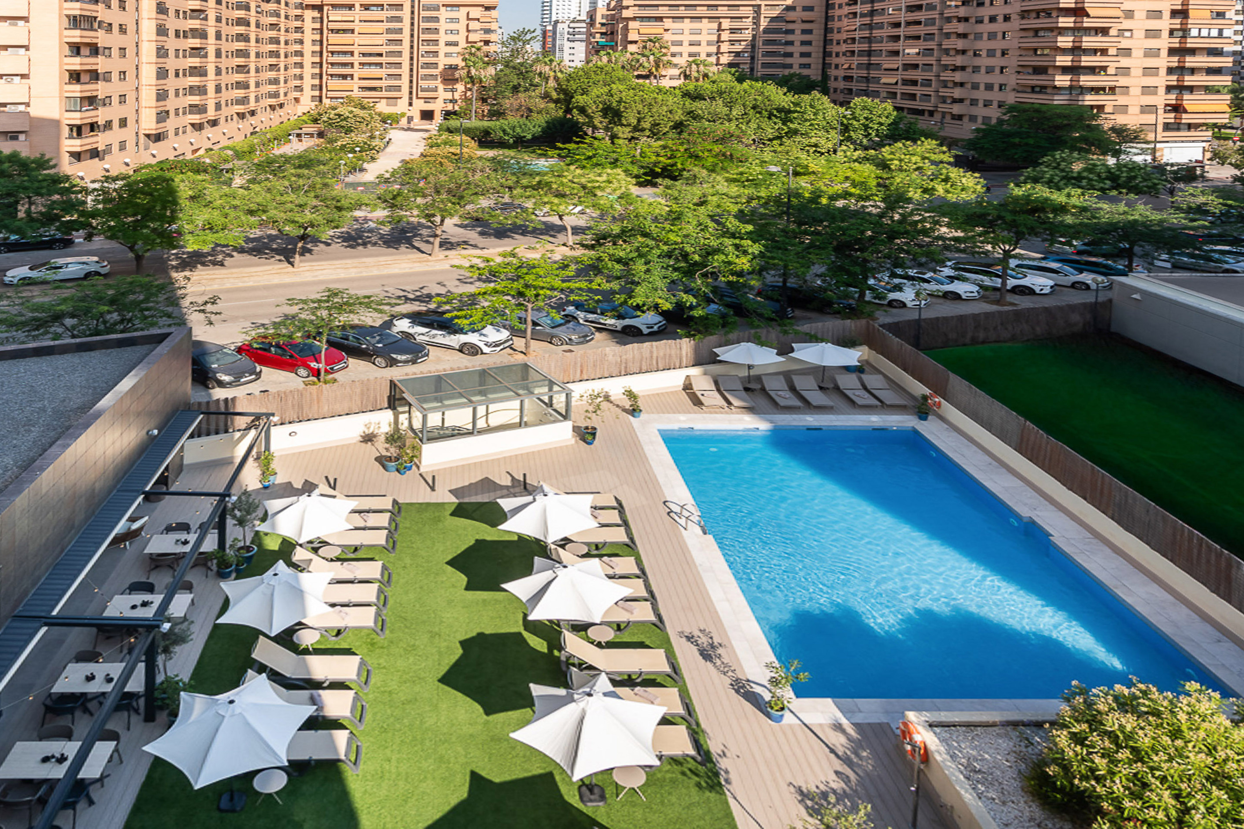 Hotel outdoor swimming pool, lounge chairs, dining area, and urban buildings.