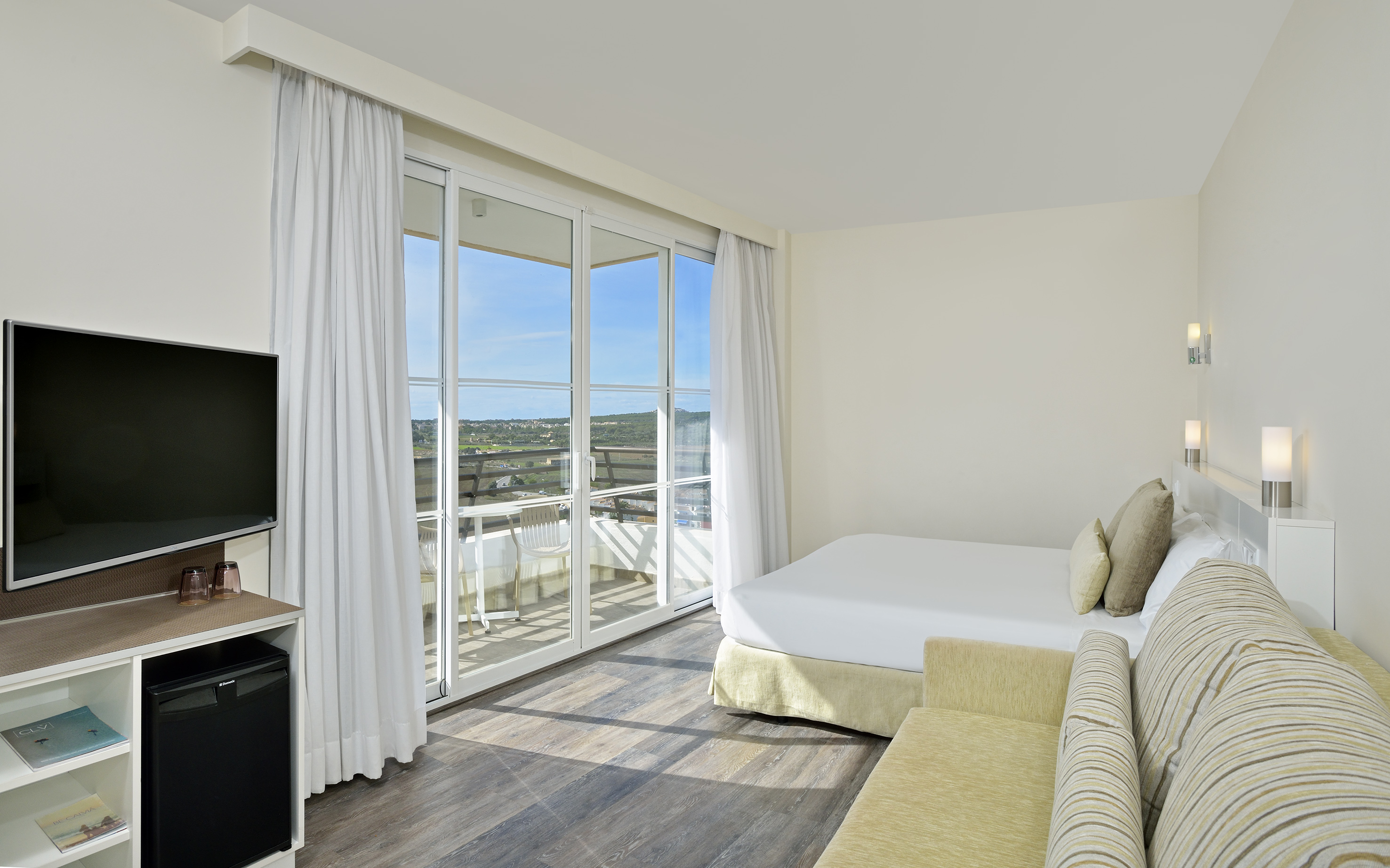 Bright modern hotel room with balcony, scenic view, bed, and sofa.