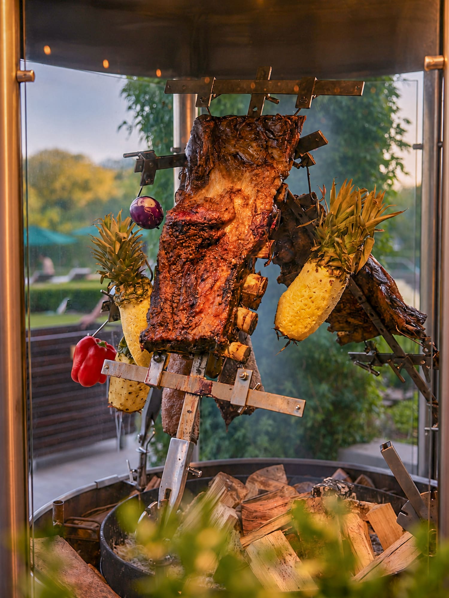 Costillas de res, piñas y verduras asándose al espeto sobre fuego de leña.
