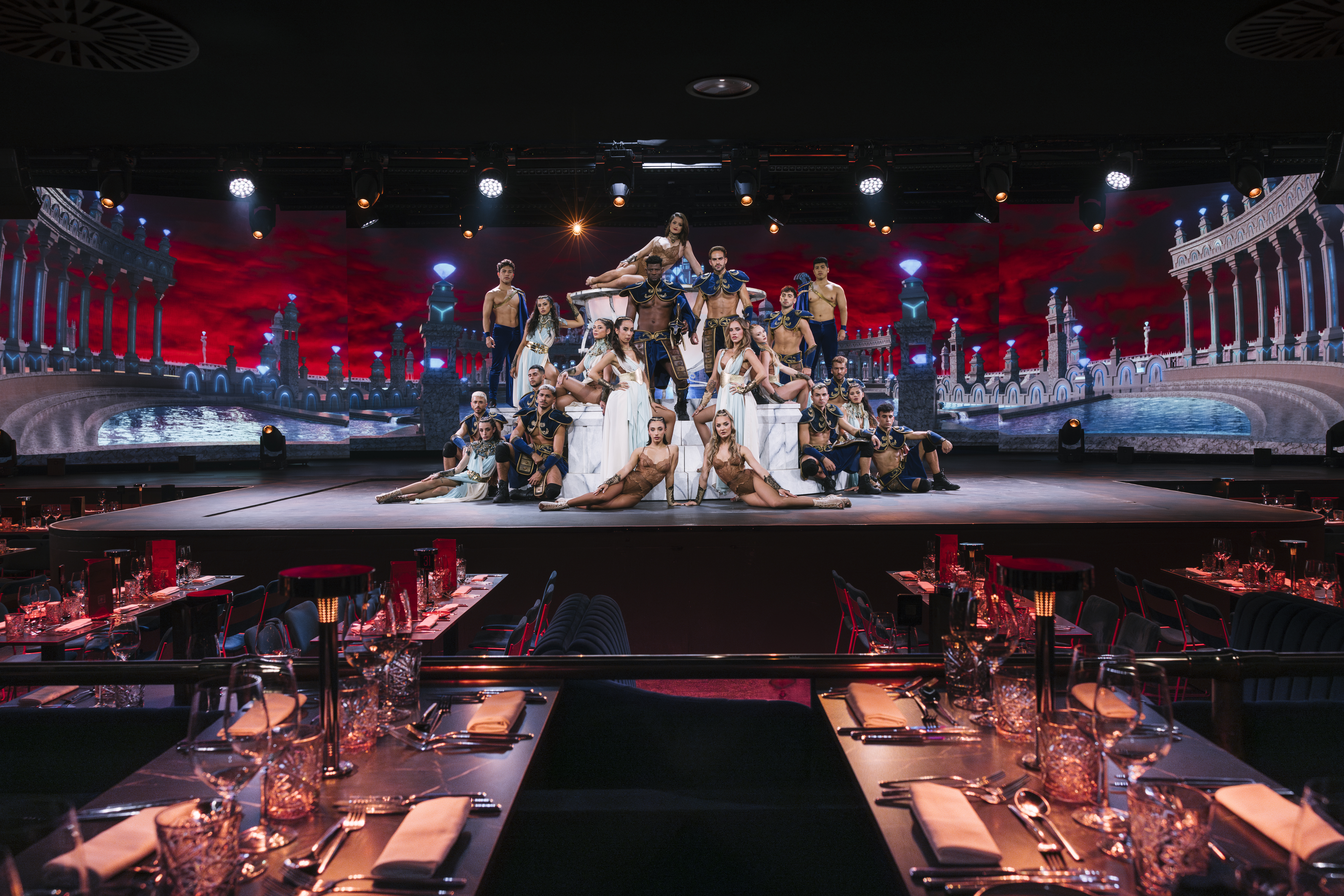 Costumed performers on stage at a dinner show, ancient city backdrop.