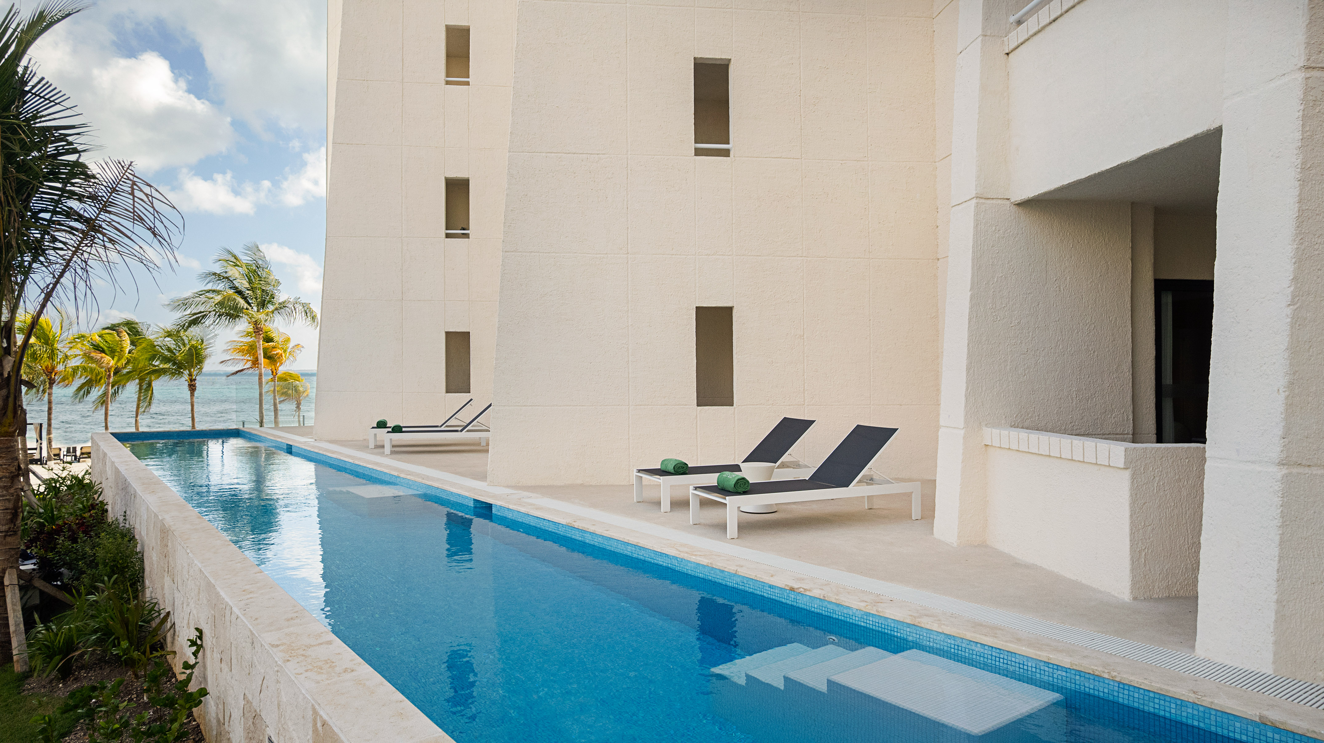 Tropical resort lap pool, ocean view, palm trees, and sun loungers.