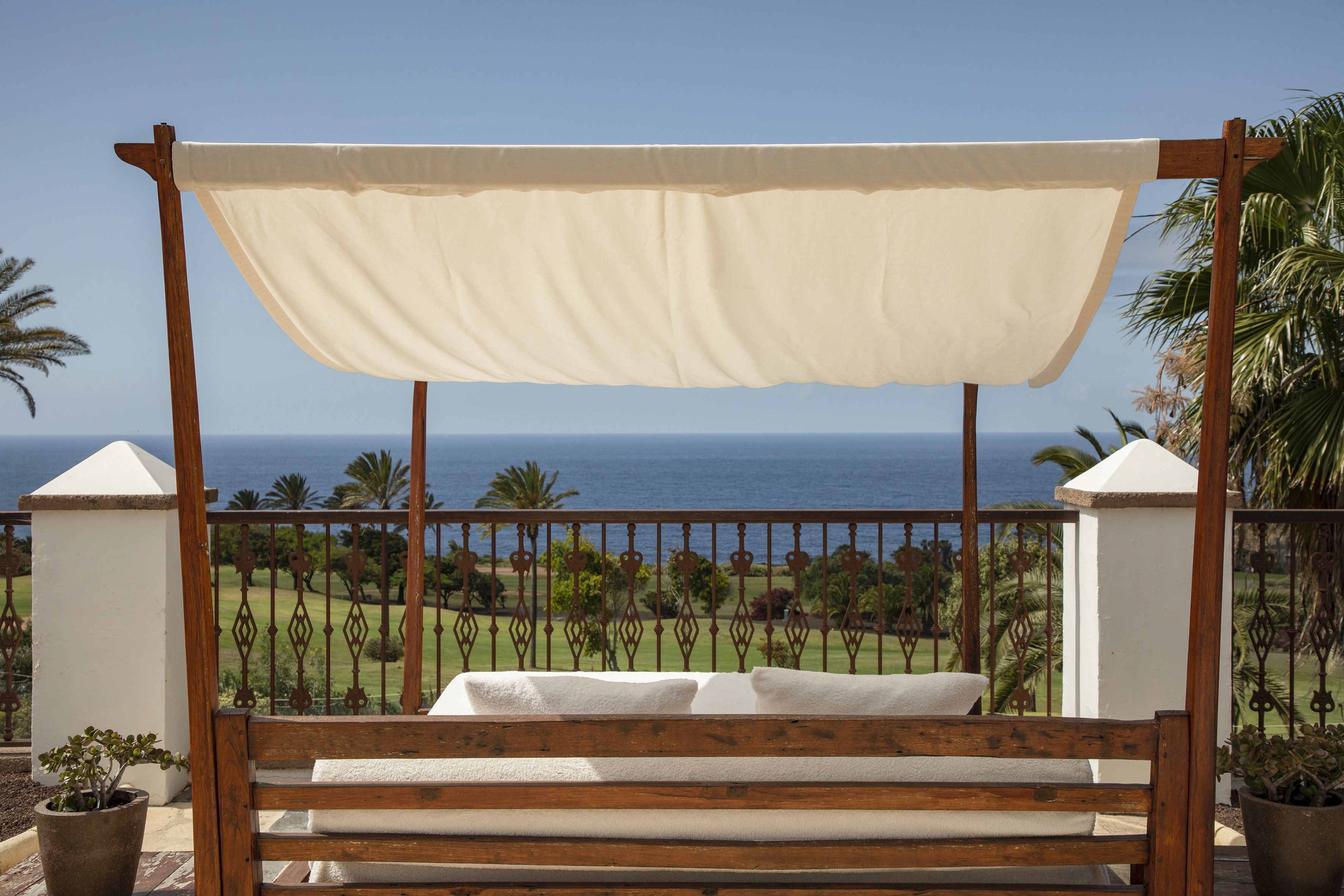 Wooden daybed with canopy overlooking ocean and green golf course from a terrace.