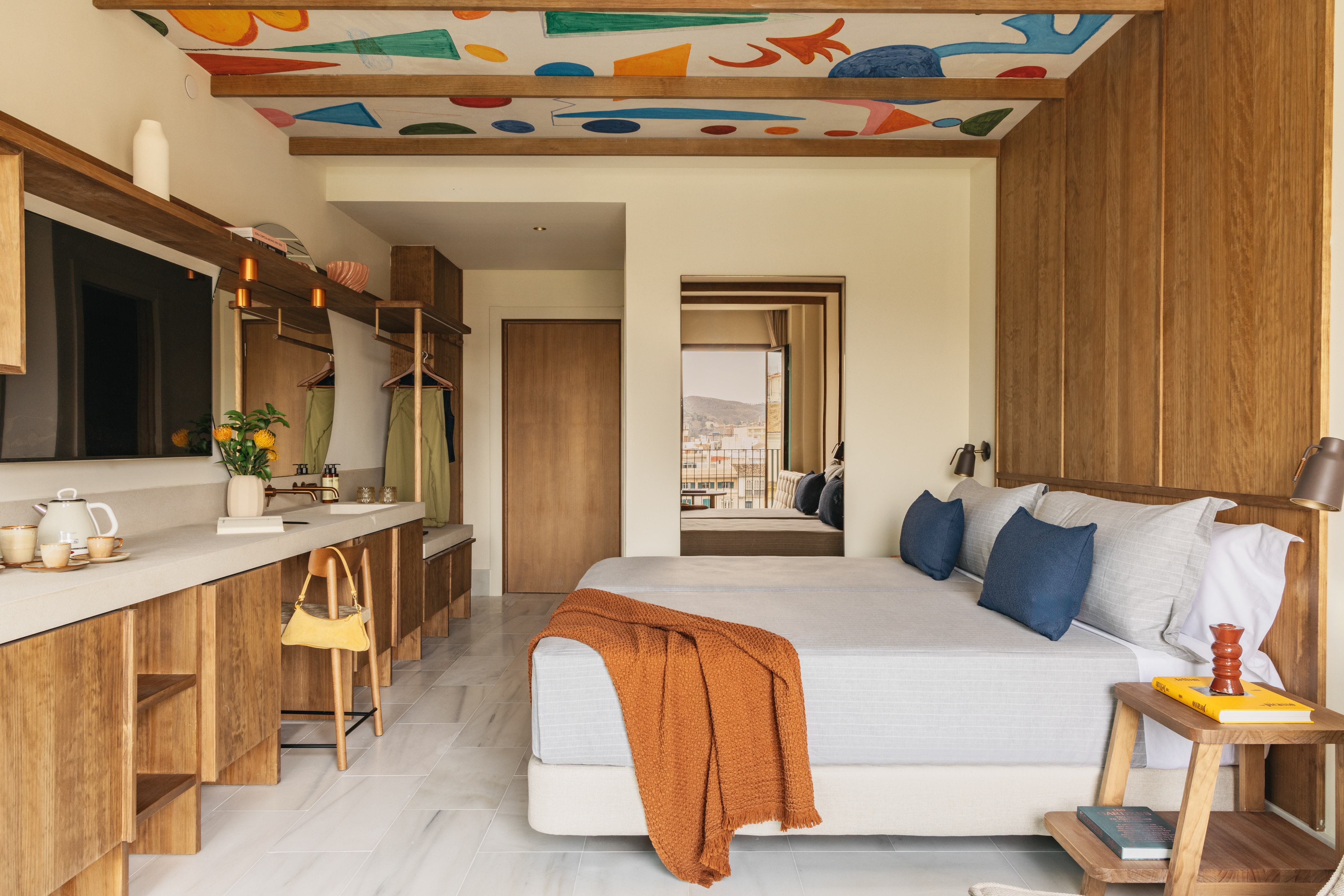 Modern hotel room with abstract ceiling art, wood accents, and balcony view.