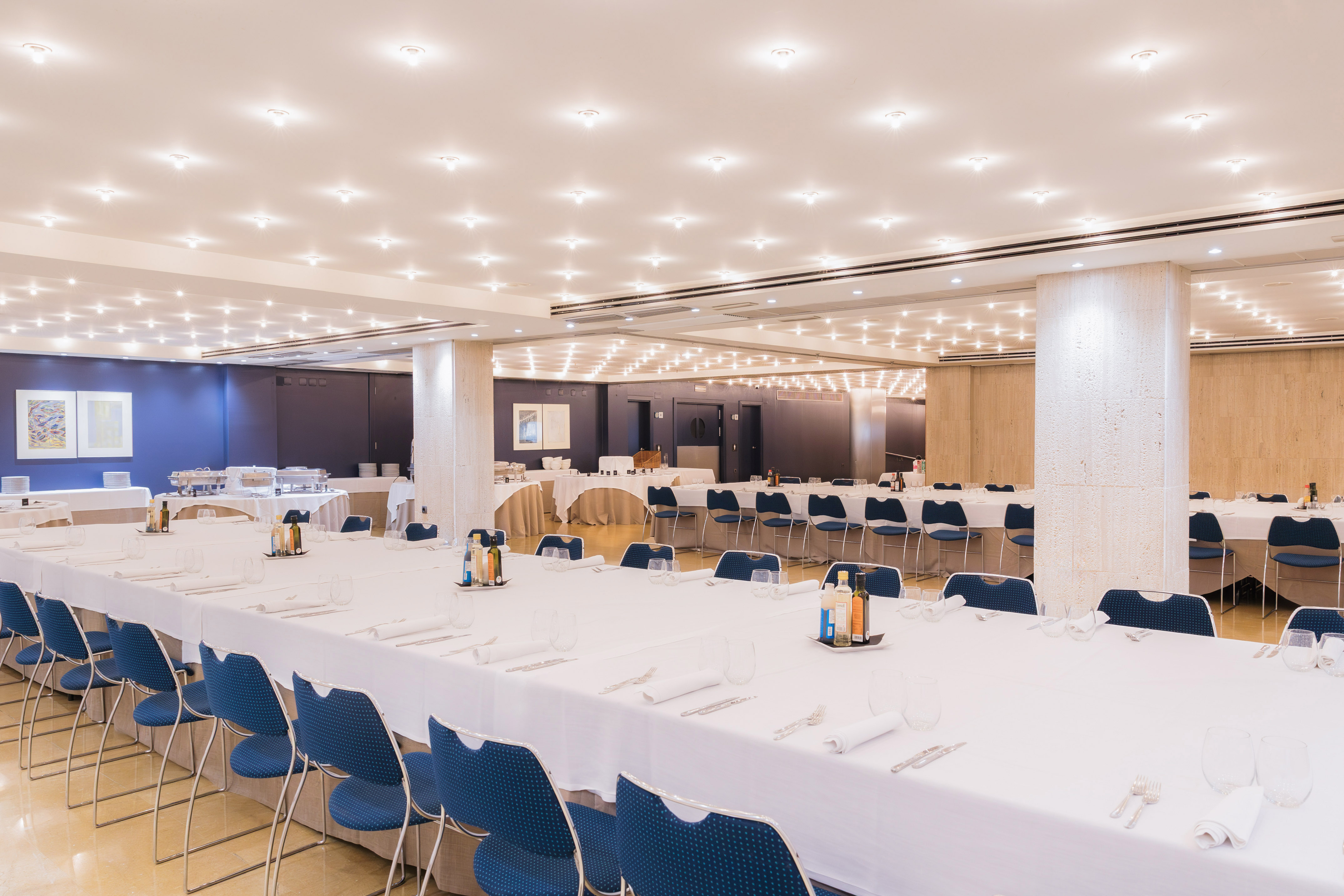 Conference event room with long white tables, blue chairs, and buffet catering.