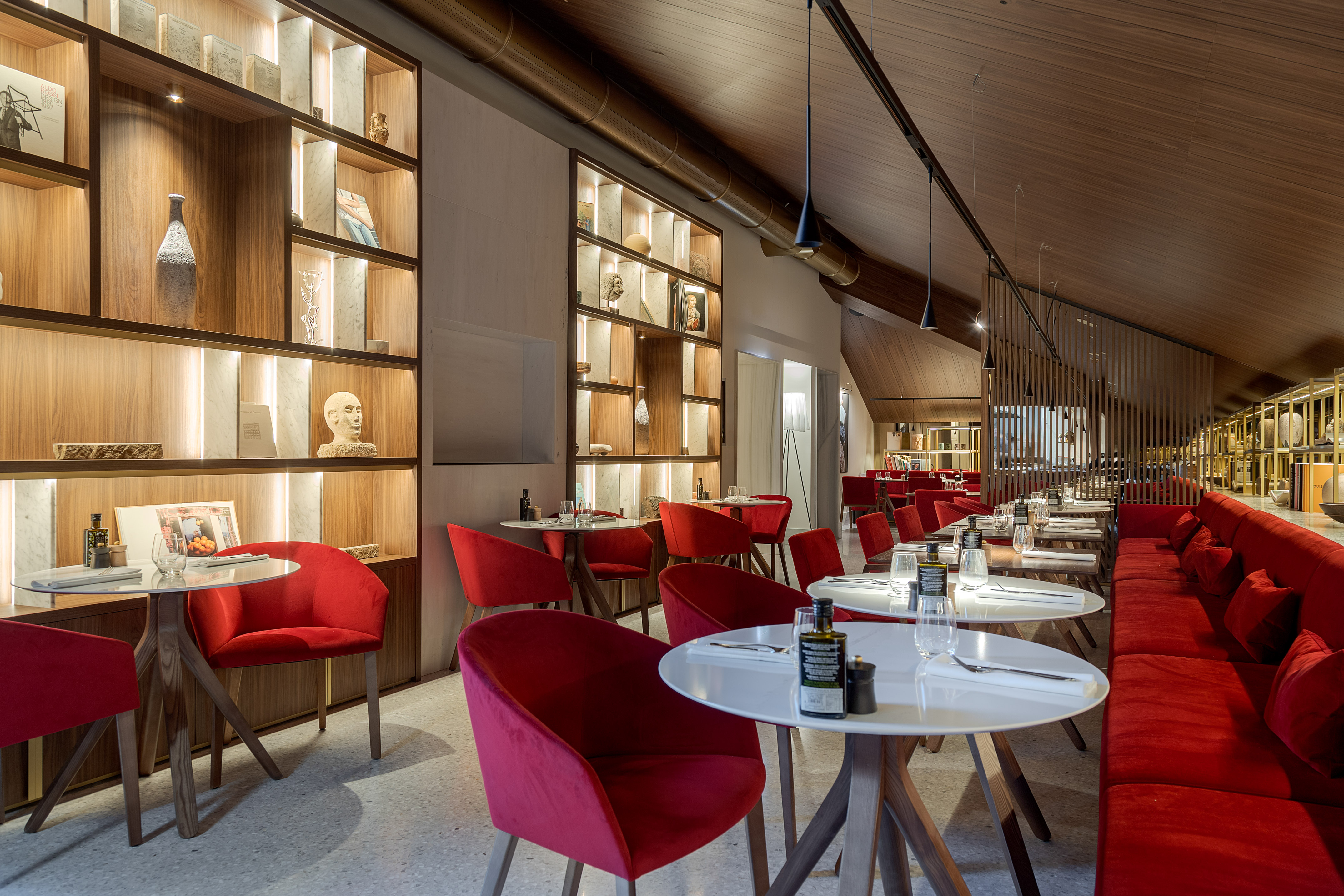 Restaurant interior: red velvet chairs, white tables, illuminated wood shelves.