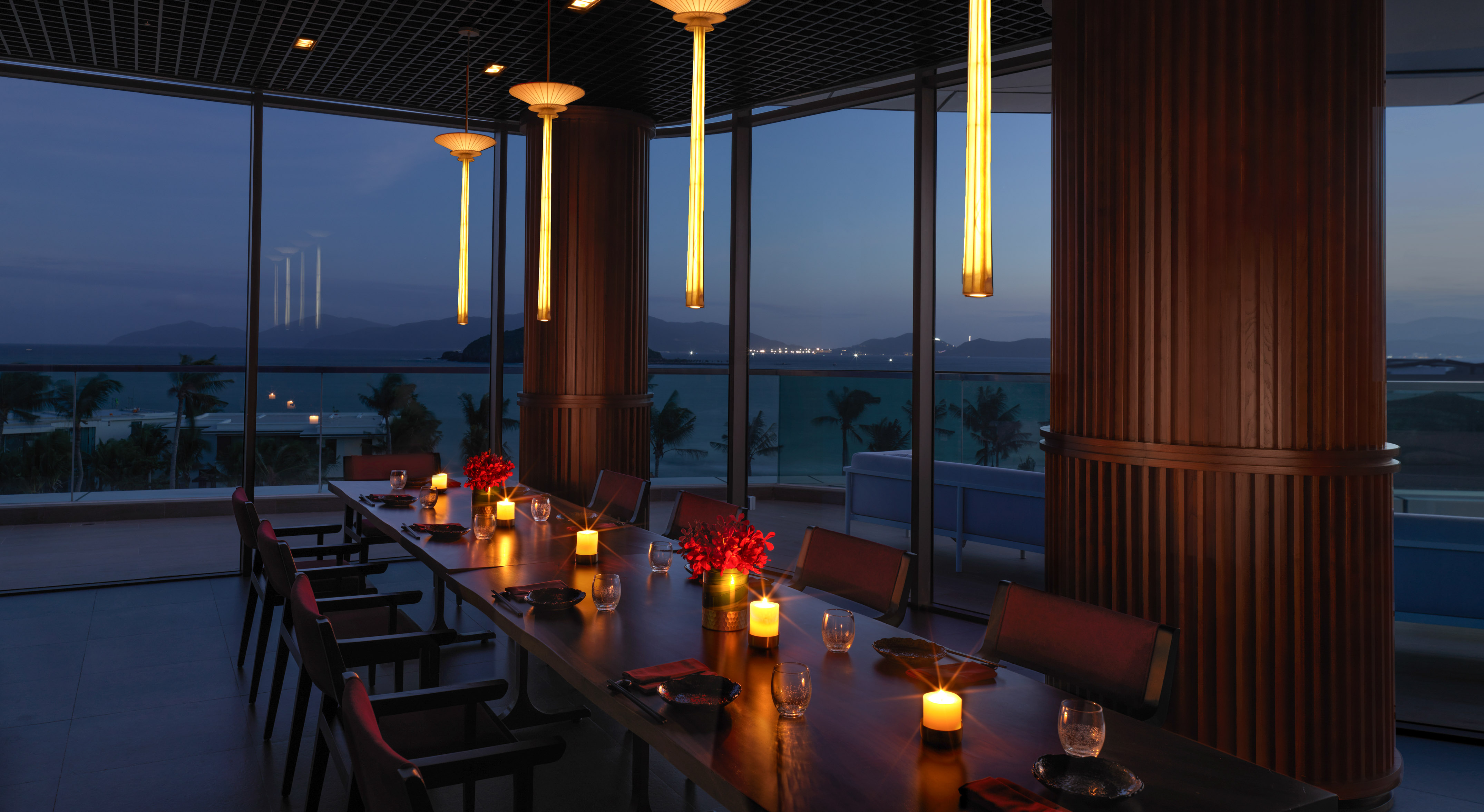 Elegant dining room, ocean view, long table with candles, evening city lights.