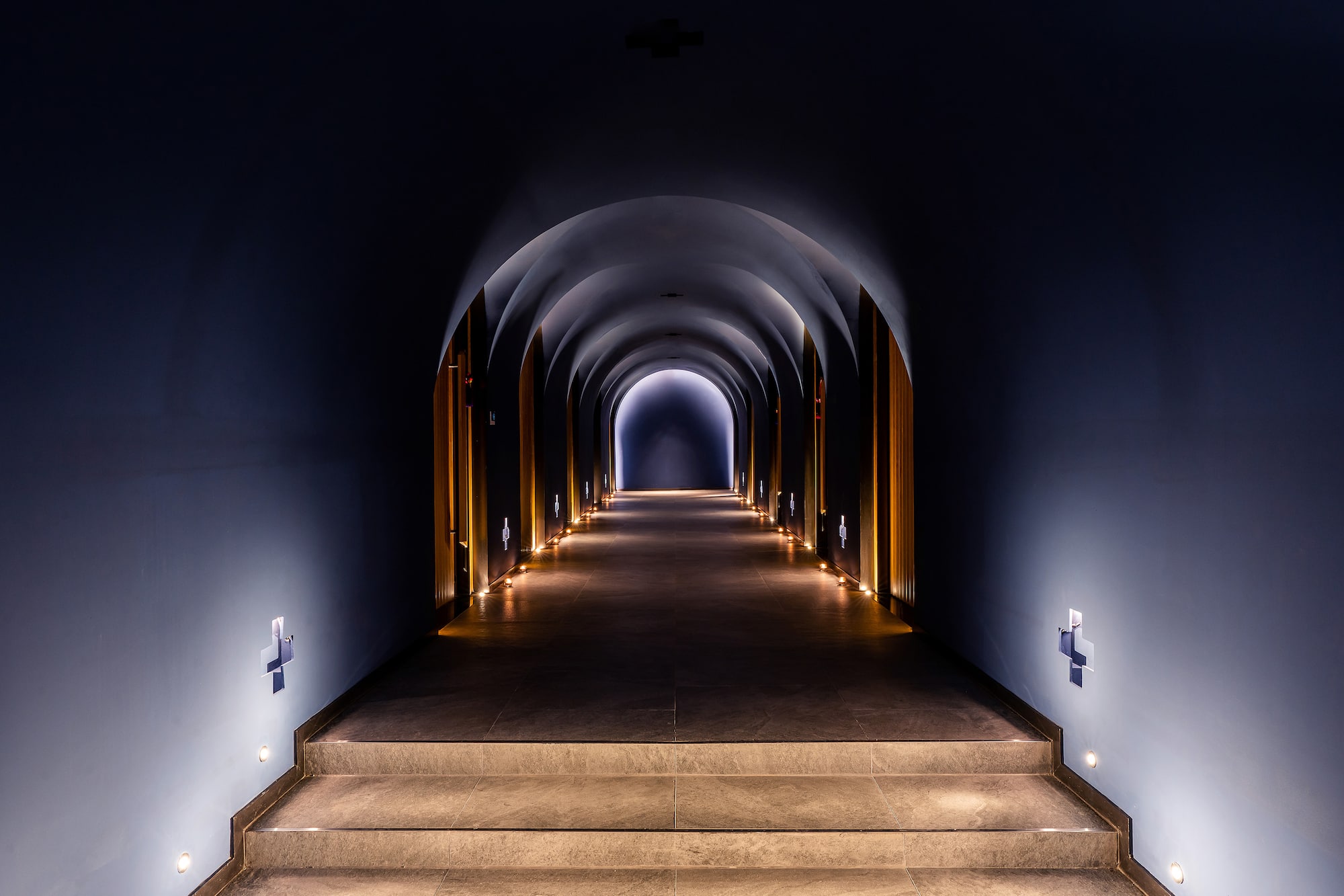 Dark arched tunnel with illuminated steps, warm accent lighting, and bright exit.