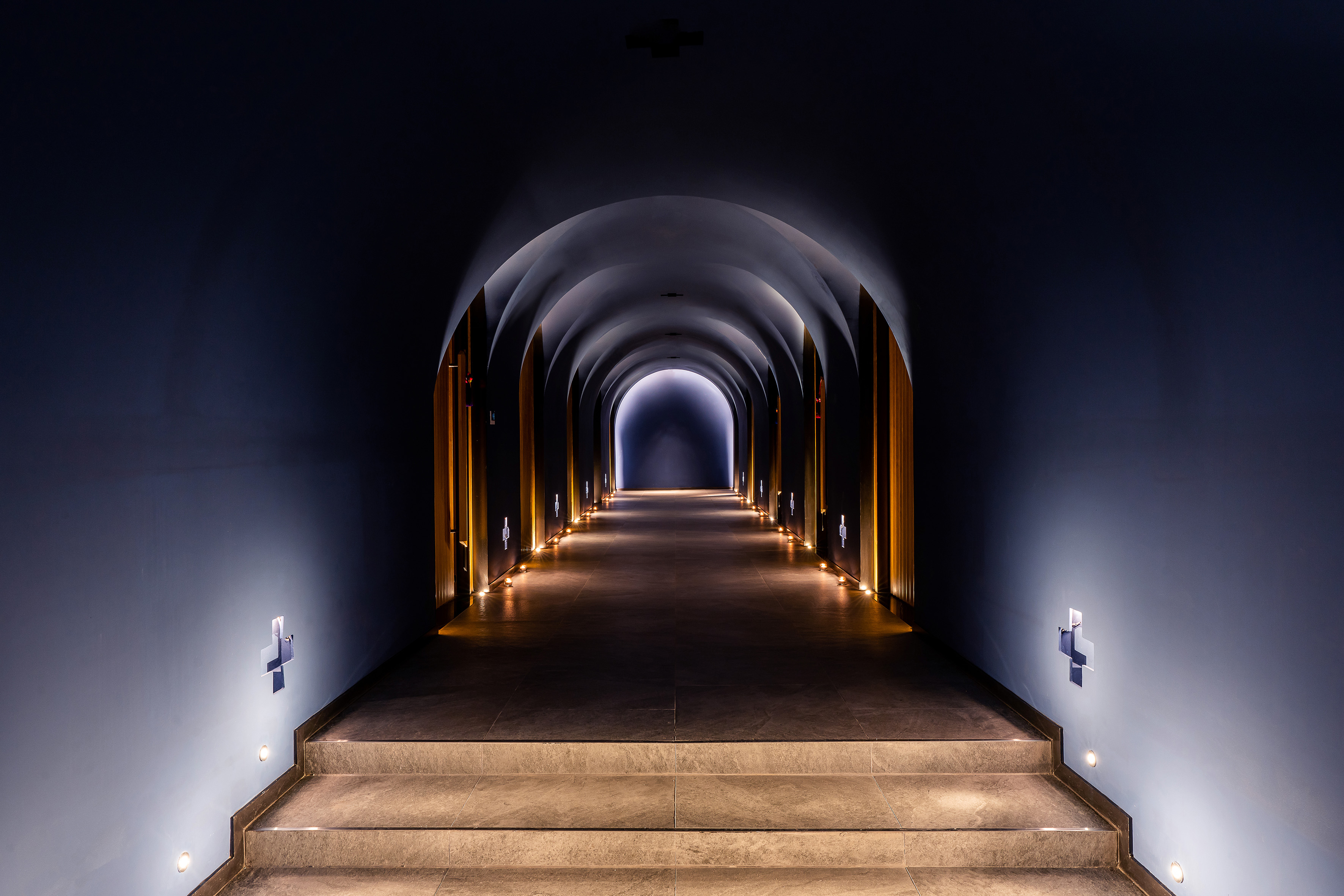 Dark arched tunnel with illuminated steps, warm accent lighting, and bright exit.