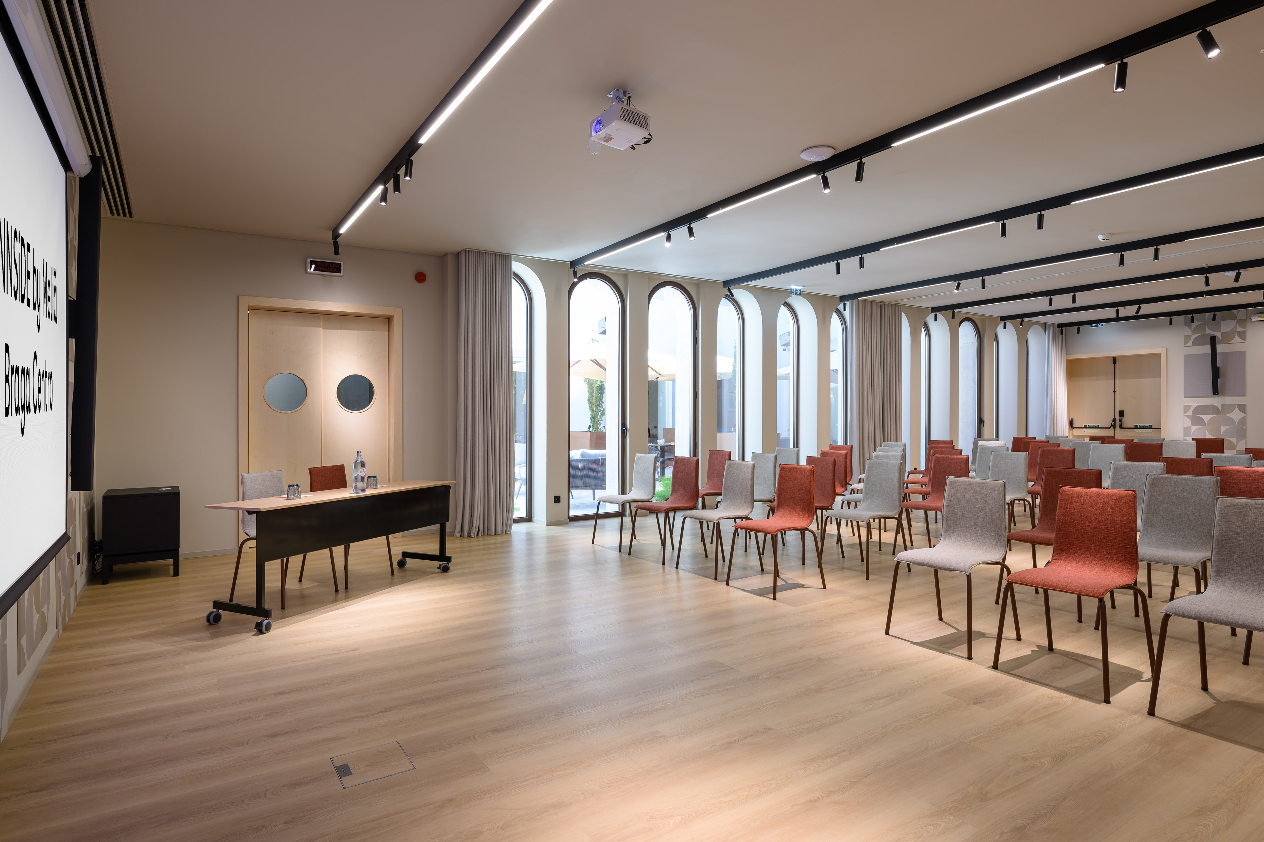 Bright conference room with projector screen, seating, and arched windows.