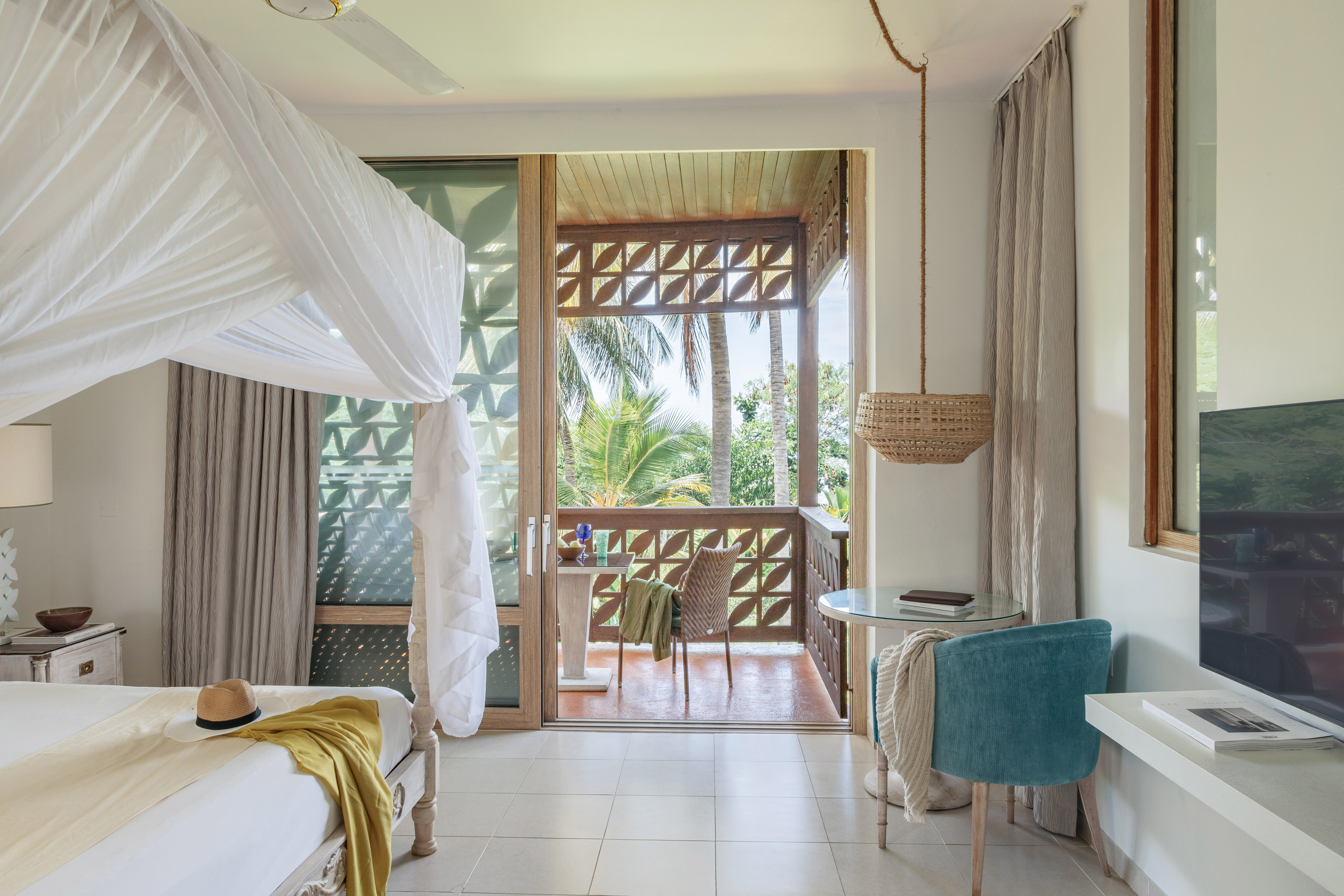 Tropical hotel room with canopy bed and balcony overlooking palm trees.