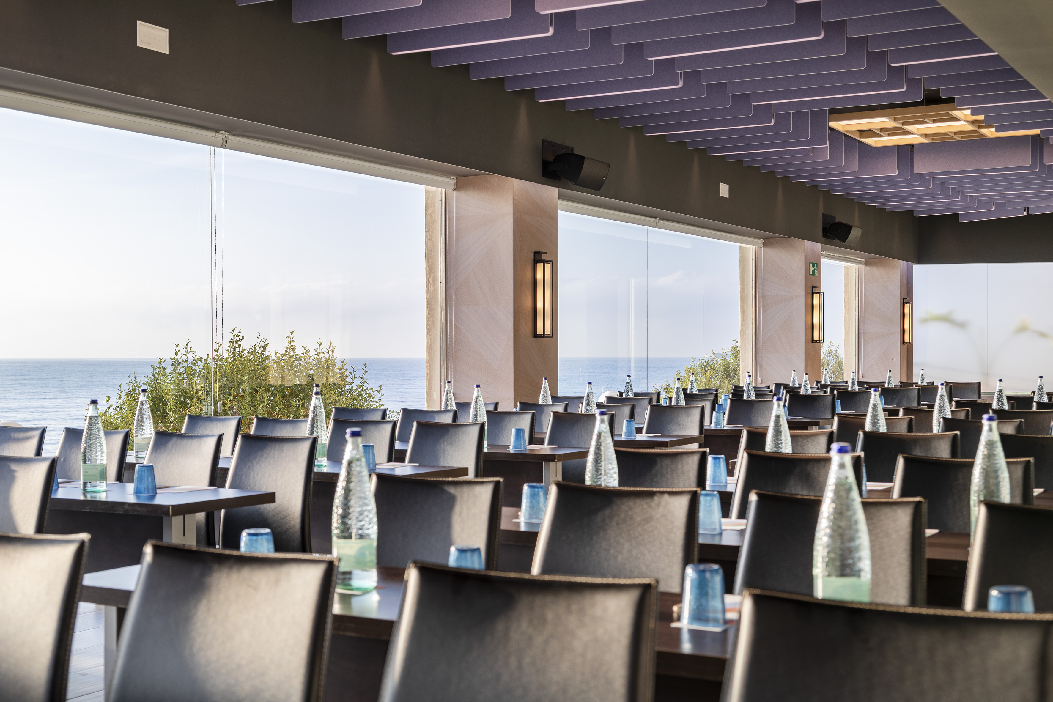 Modern ocean view meeting room with classroom setup tables and chairs.