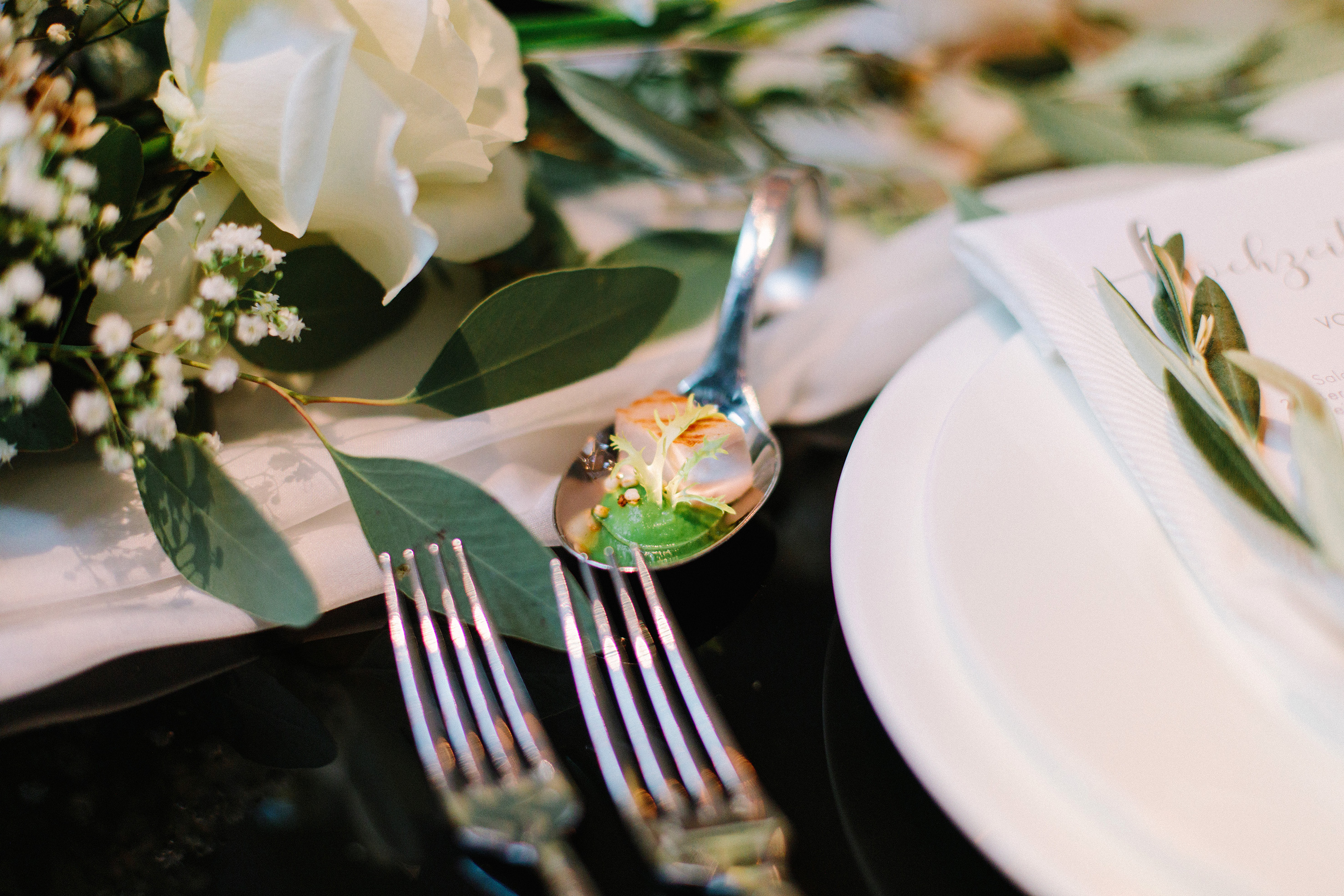 Elegant dining table setting with appetizer spoon, white roses, eucalyptus, and menu.