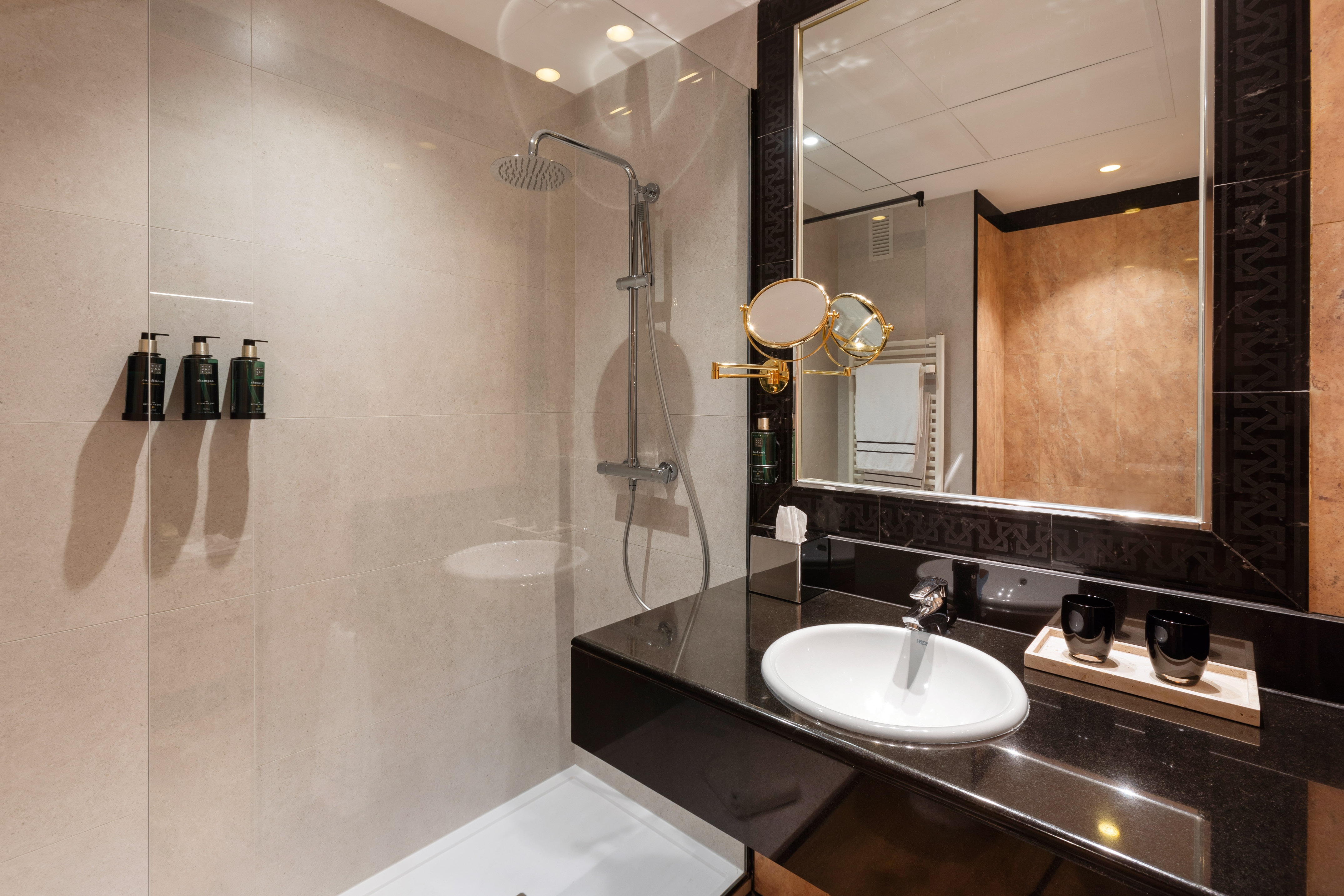 Modern hotel bathroom: rainfall shower, black vanity, white sink, and mirror.