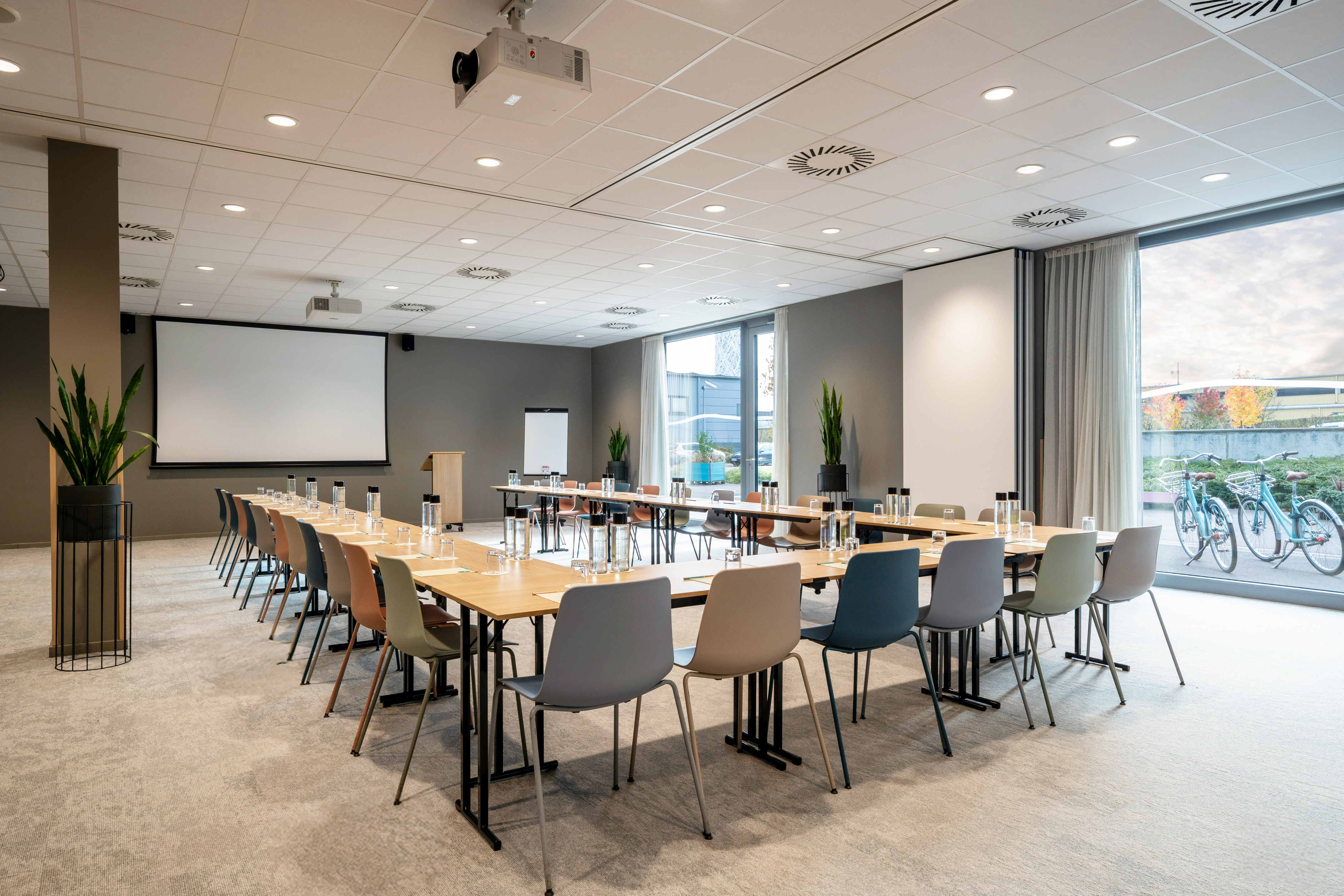 Modern U-shaped conference room setup with projector screen and natural light.