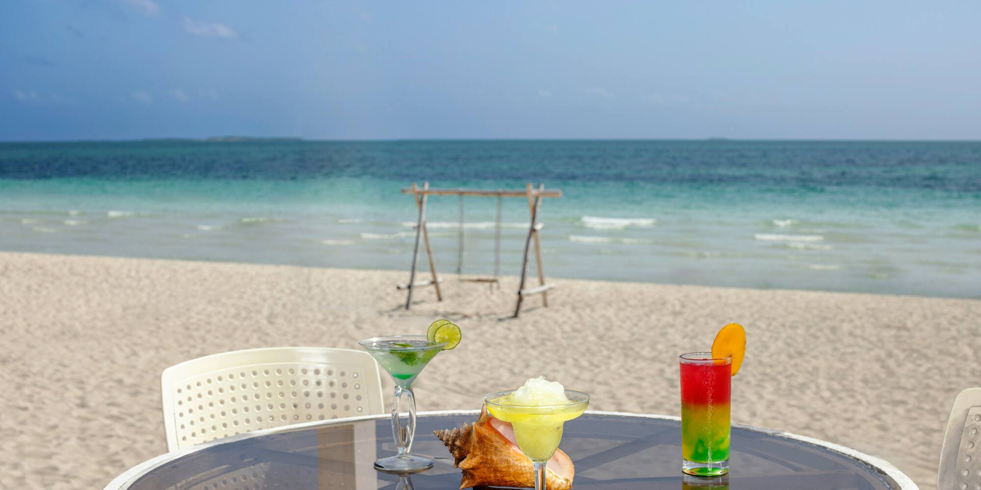 a table with drinks on it and a swing on the beach