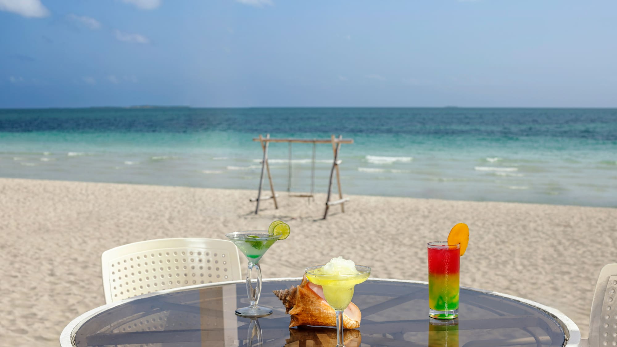 a table with drinks on it and a swing on the beach